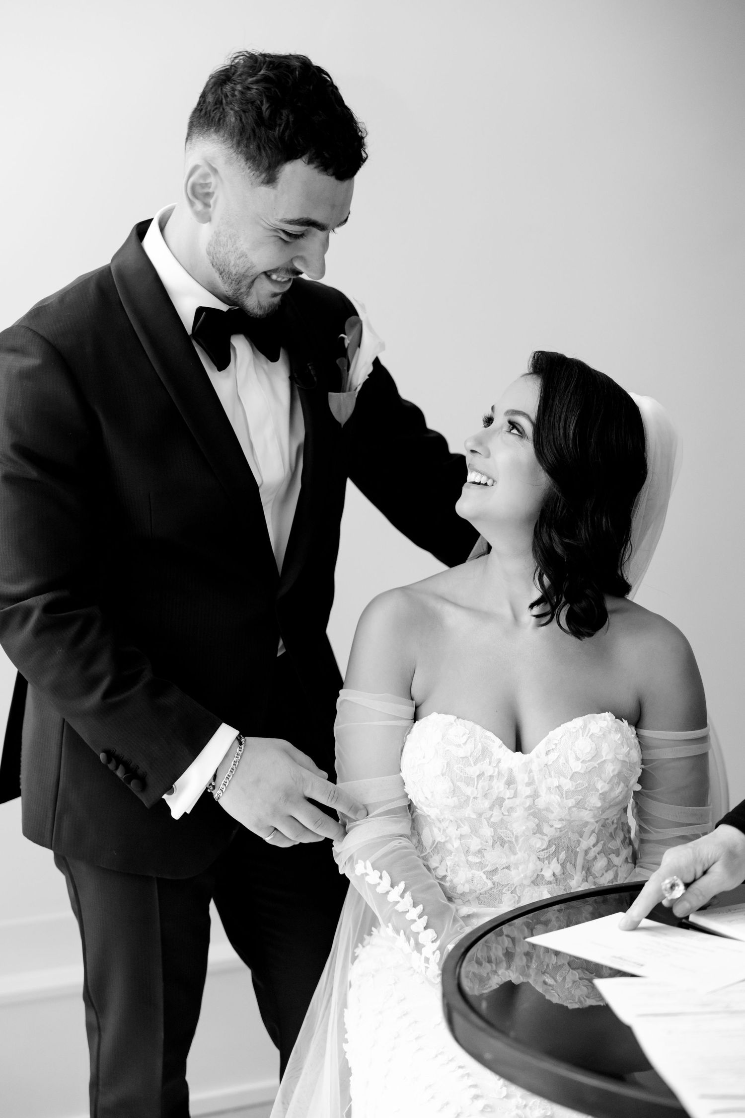 Black and white portrait of couple sharing intimate moment while signing marriage documents.