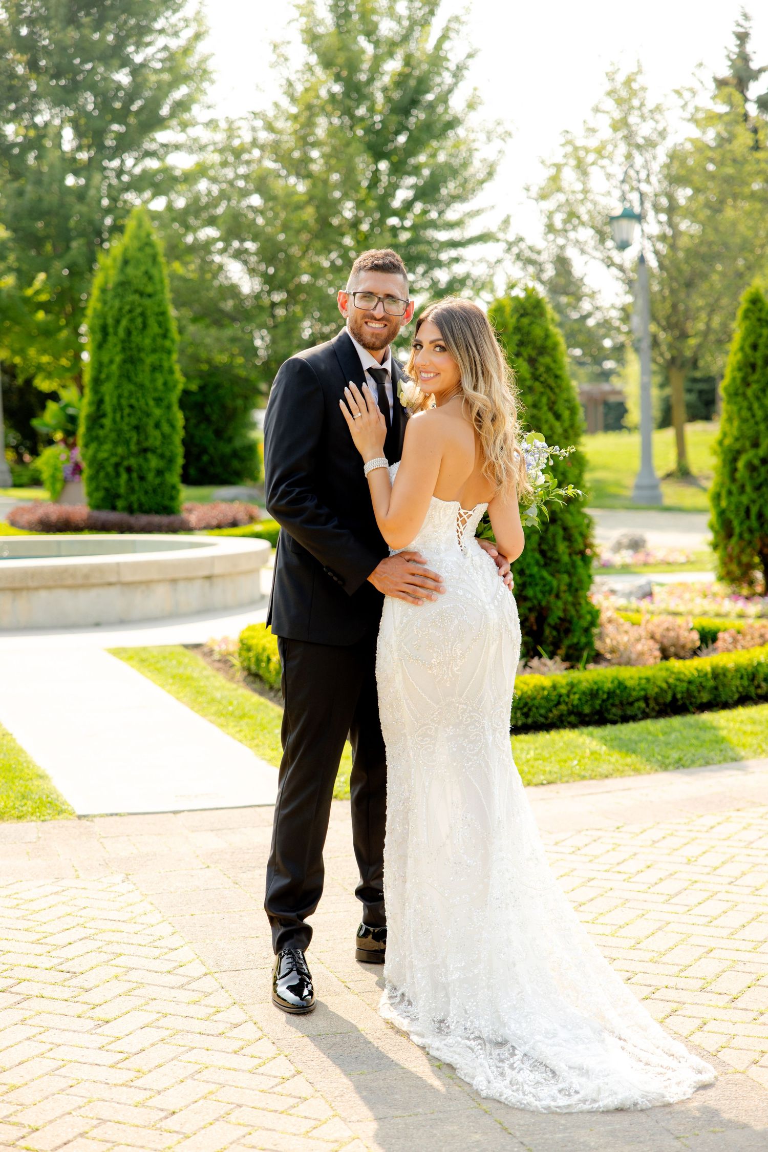 Joyful wedding couple posing together on garden path with bride showing off lace gown details.
