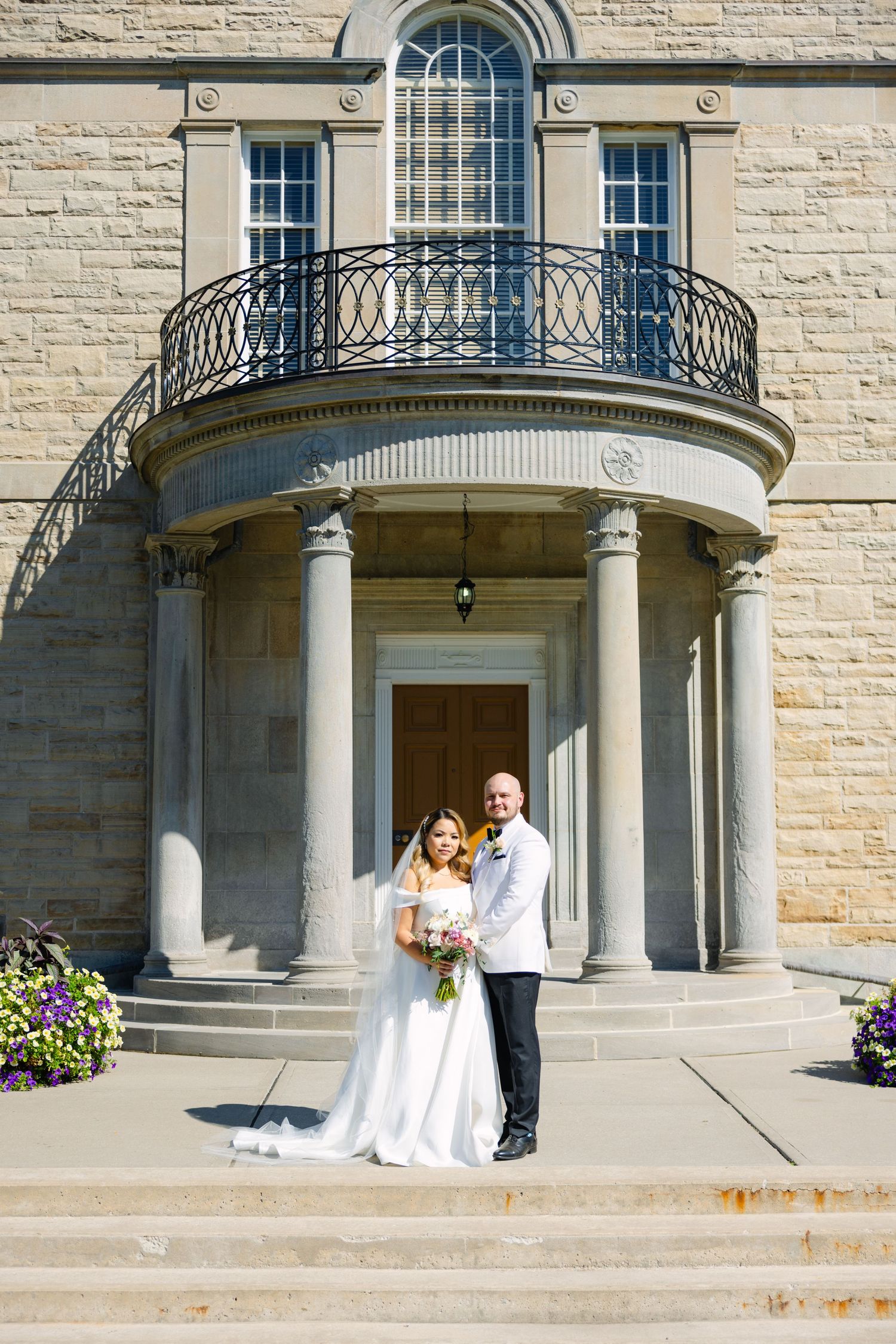 Wedding couple poses under columned portico of elegant stone building.