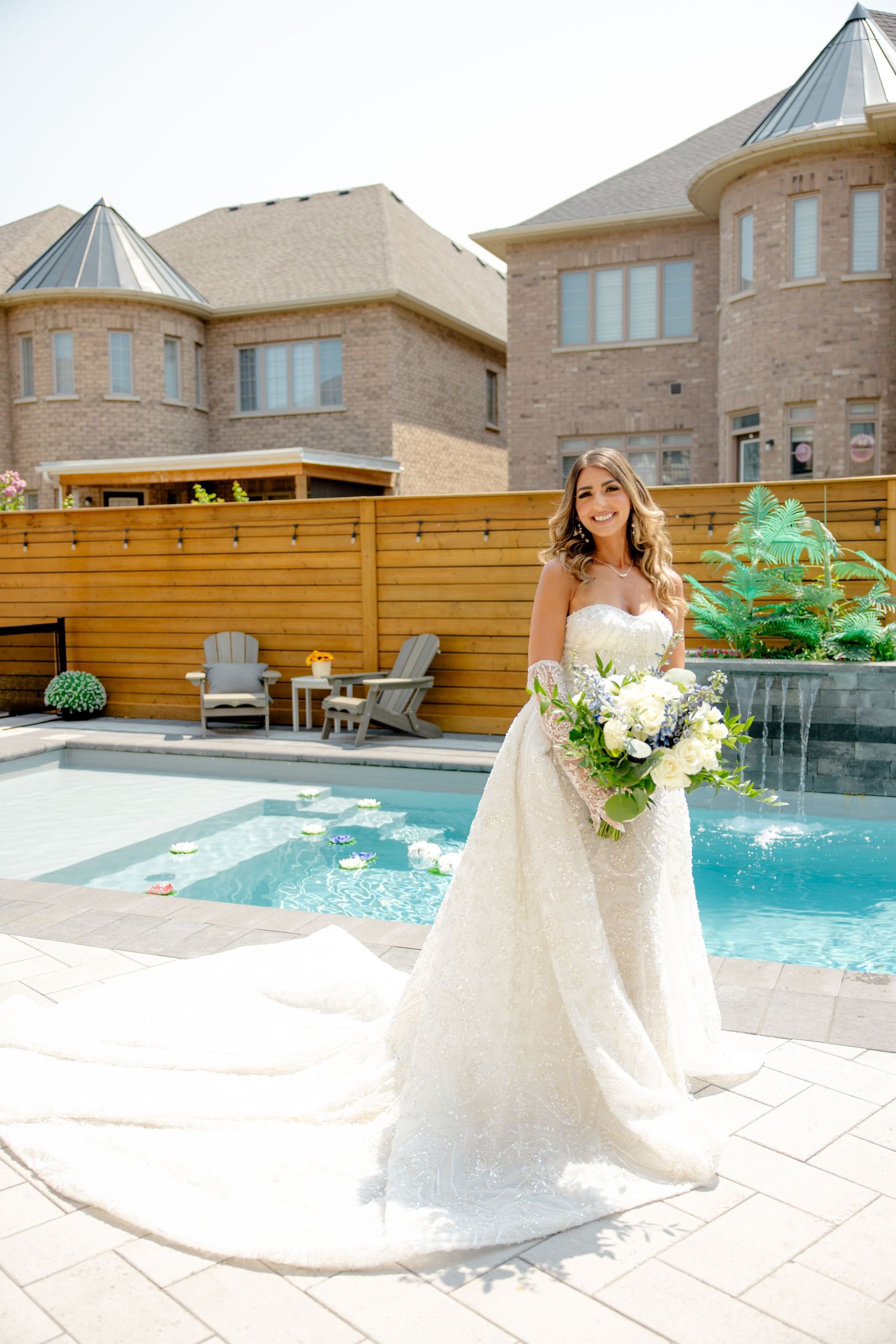 Elegant bridal portrait by a pool with stone mansion backdrop and white floral bouquet.