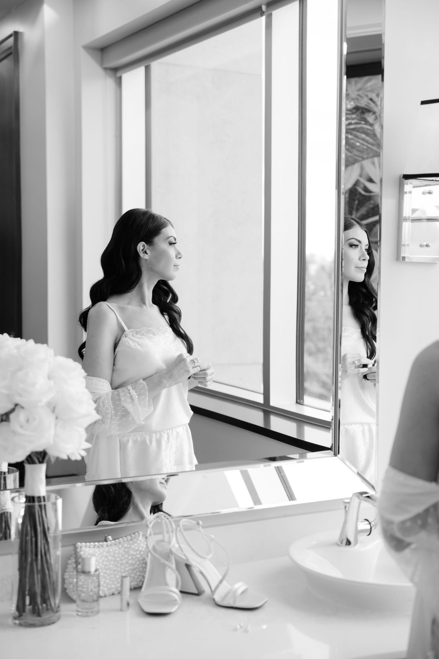 Black and white photo of bridal preparations in modern bathroom with window light.