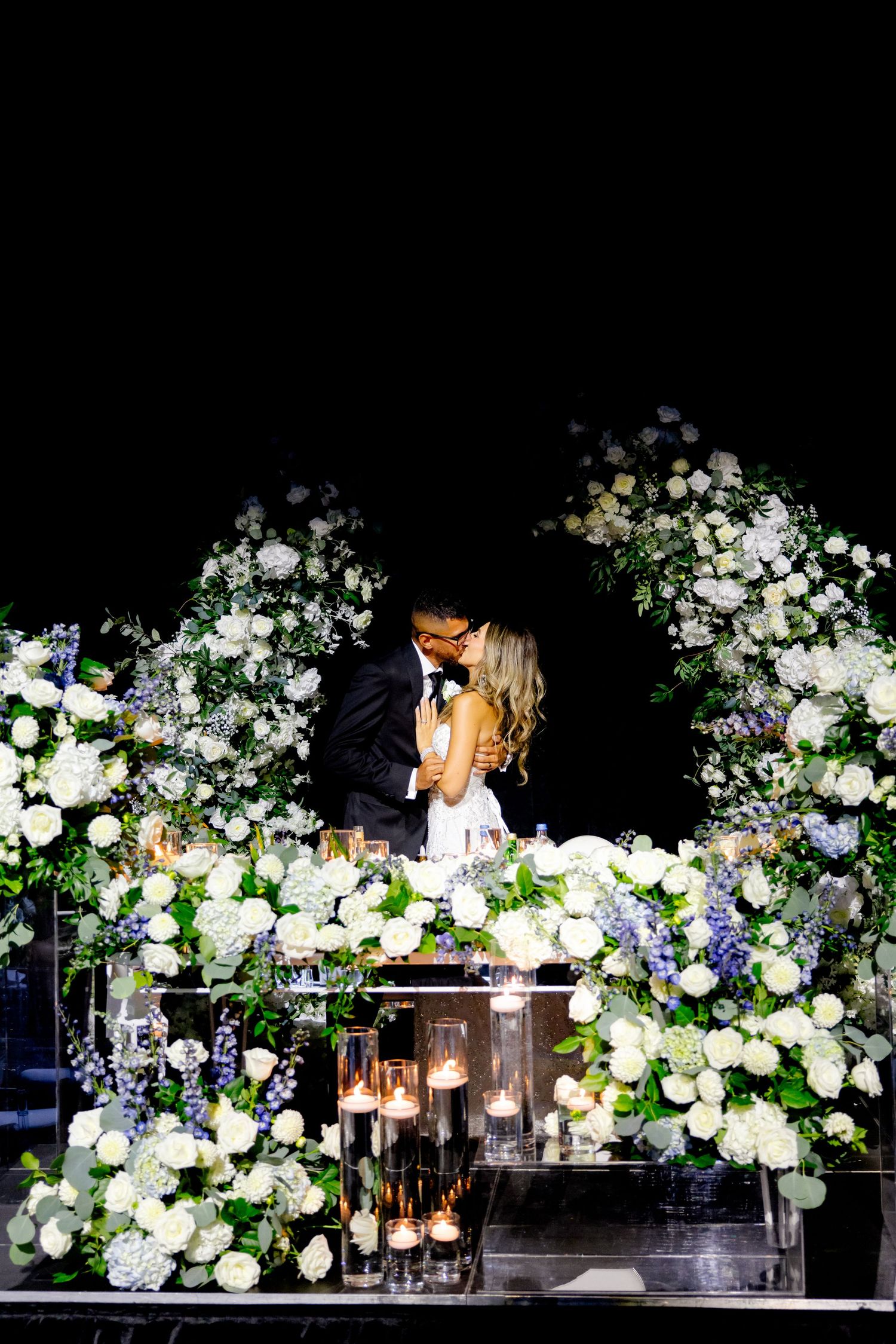 Wedding setting at night with dramatic floral arch and lanterns creating a romantic ambiance.