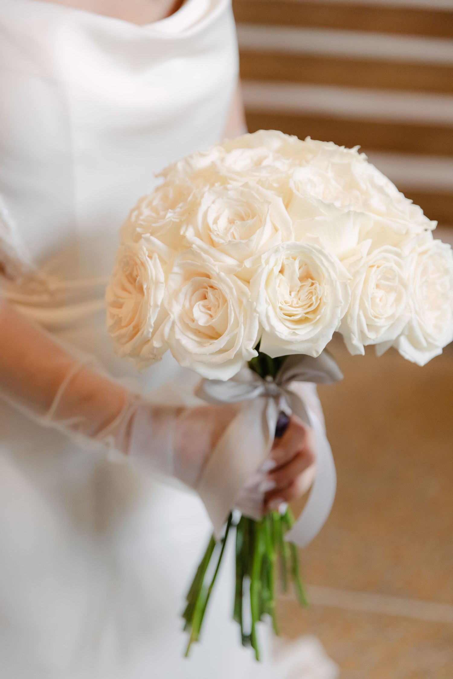 A close-up of a classic cream rose wedding bouquet with silk ribbon against a white wedding dress.