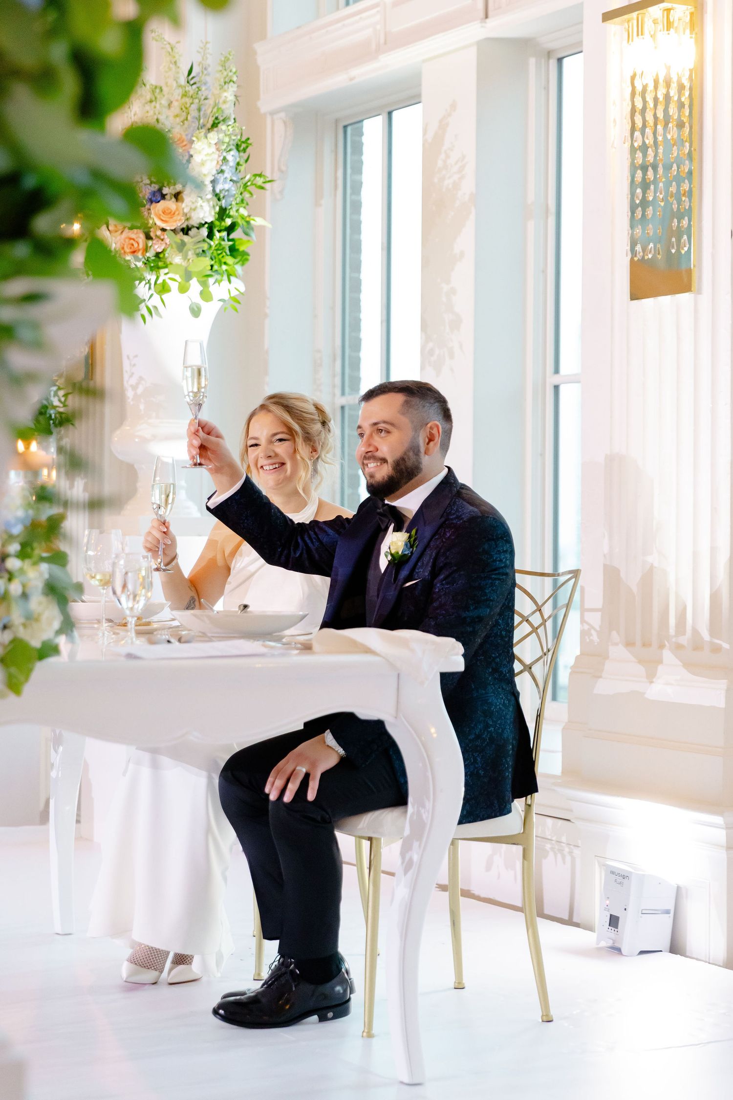 Wedding reception venue with white tables and chairs decorated with greenery and natural light.