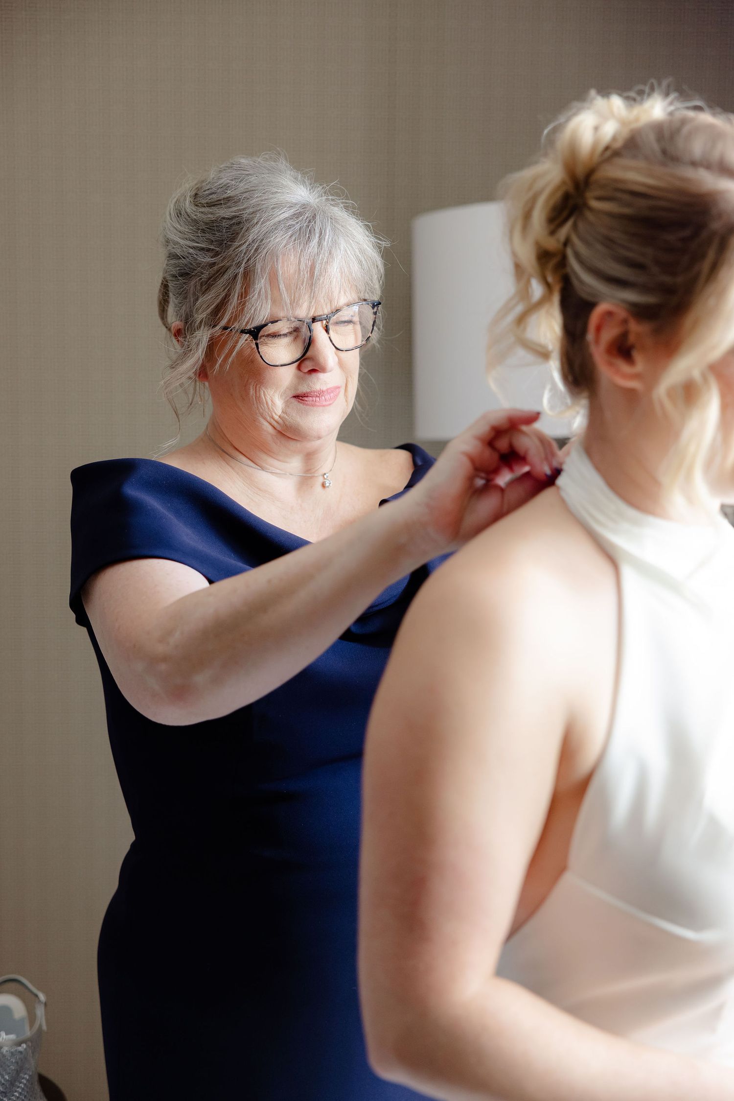 A series of photos showing someone in a navy dress helping another person get dressed in white formal attire.