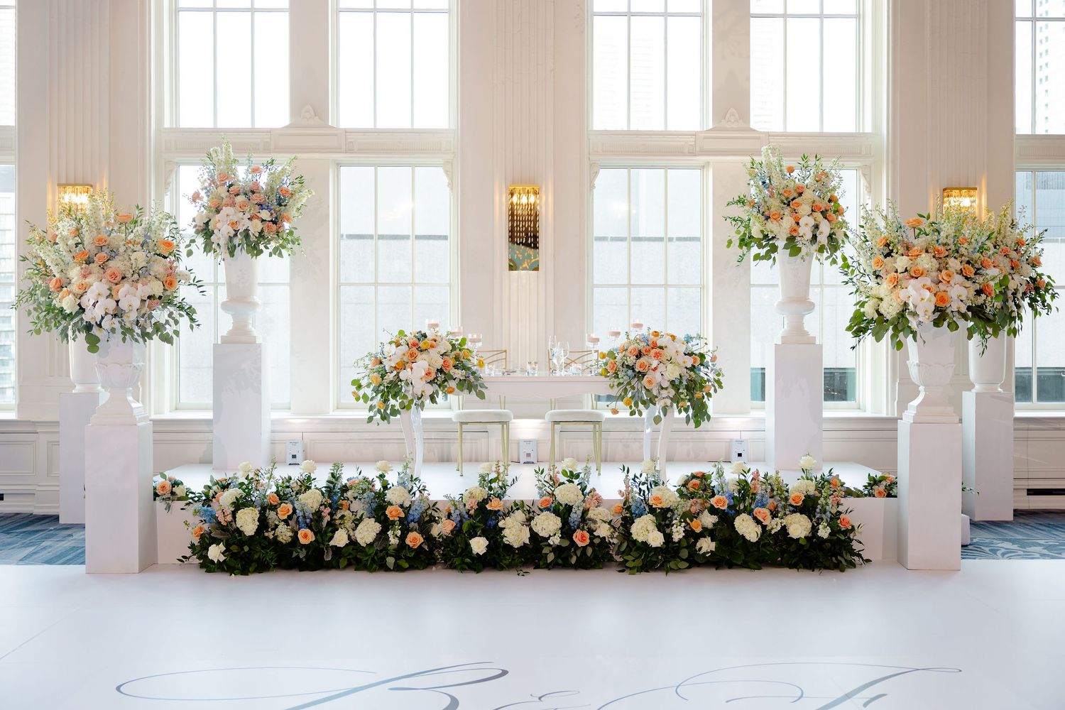 Bright white wedding reception venue with tall windows and floral arrangements lining the perimeter.