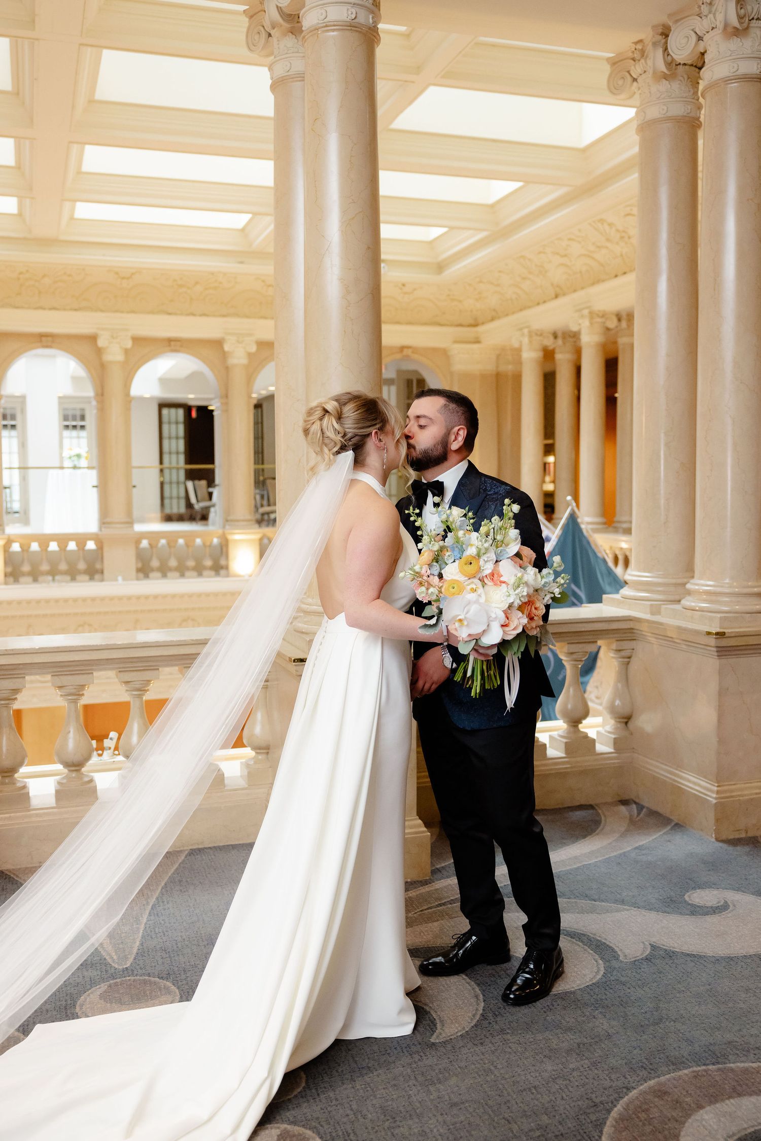 A bride and groom share intimate moments in an elegant columned hall with natural lighting.