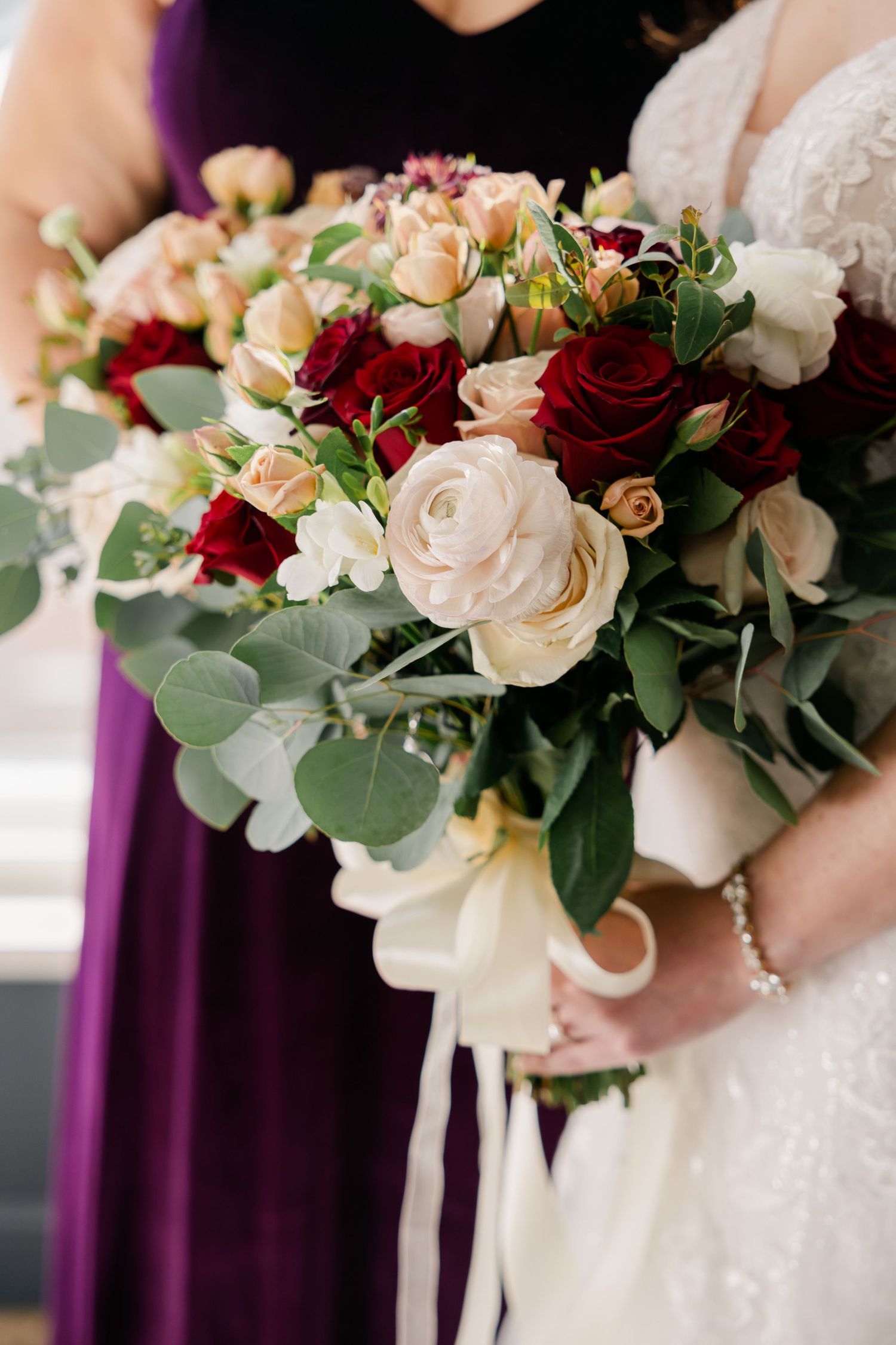 Close-up of romantic wedding bouquet featuring red and white roses with eucalyptus greenery.