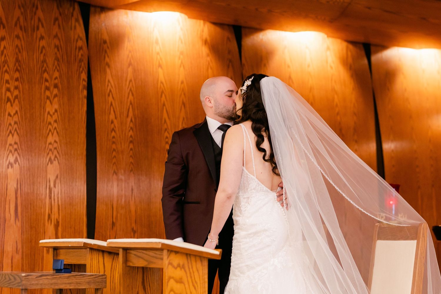 Intimate wedding moment captured against wood-paneled walls with warm overhead lighting.