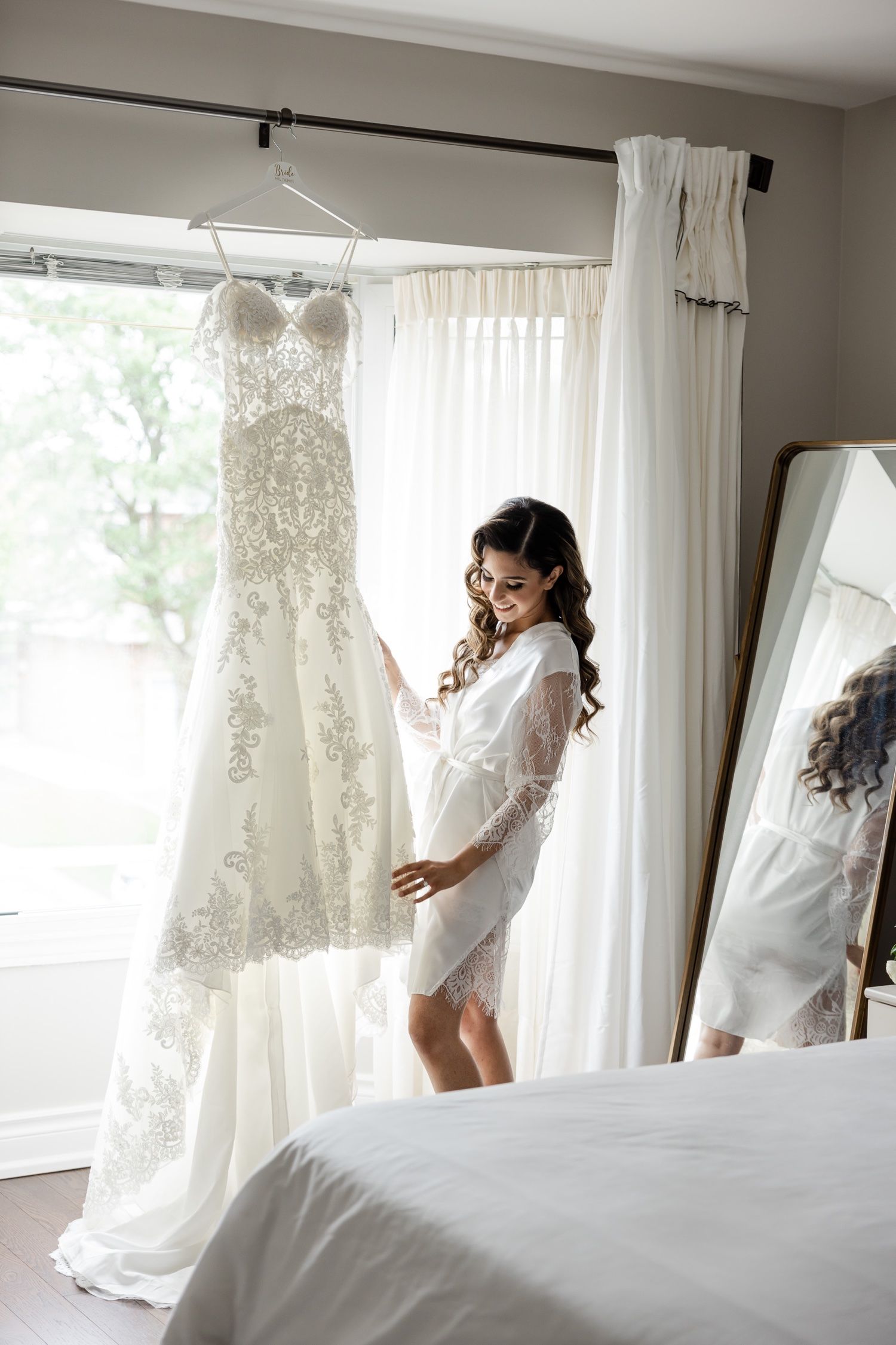 Wedding dress preparation scene with natural window light in bedroom setting.