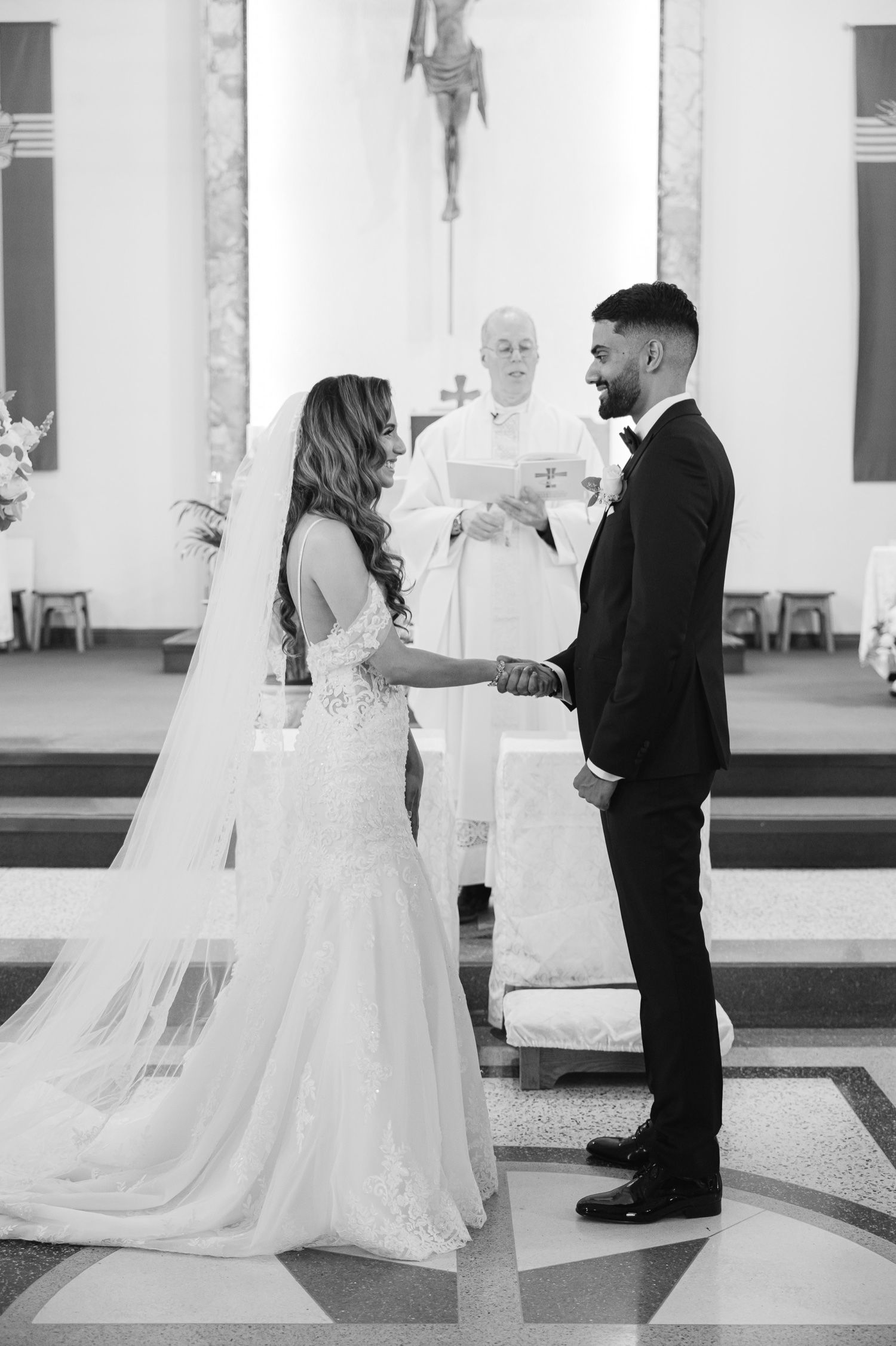 A black and white photo capturing an intimate wedding ceremony moment in a Catholic church.