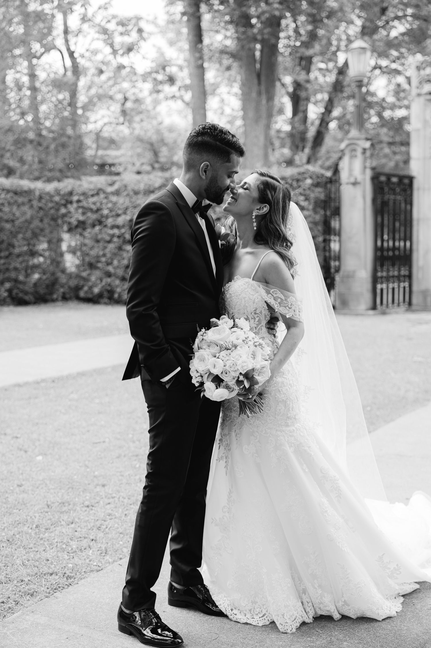 Black and white wedding portrait showing intimate moment between couple with flowing bouquet and veil.