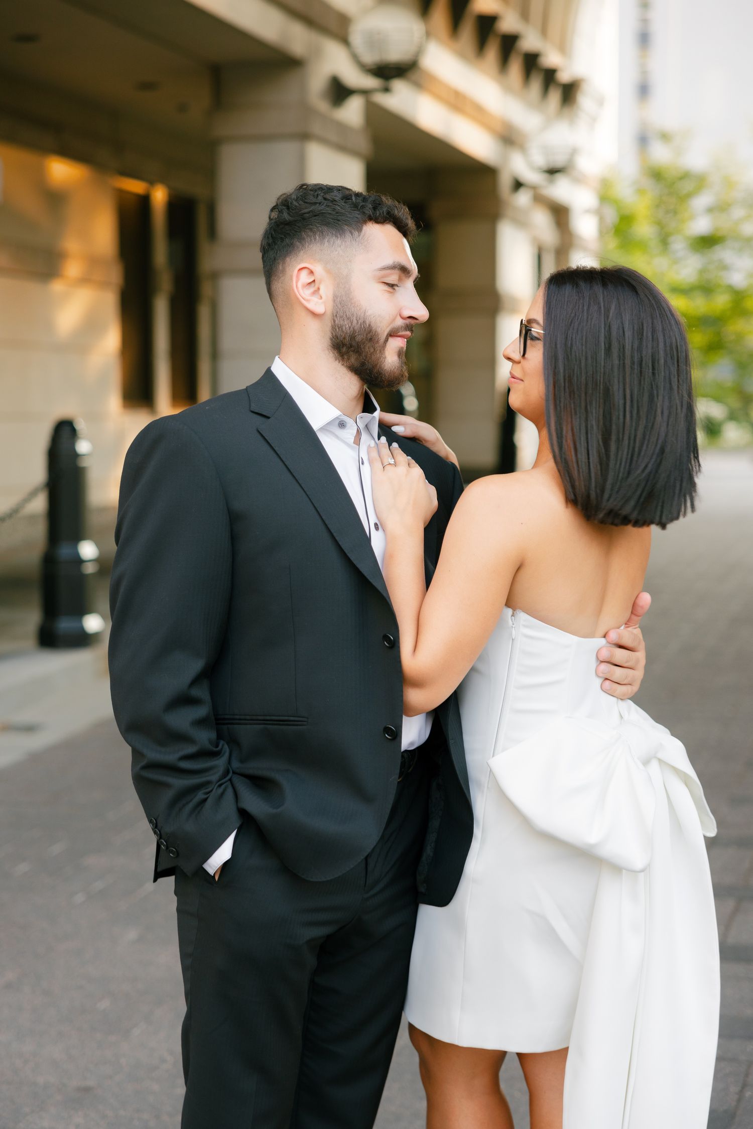 A couple shares an intimate moment in contrasting formal wear outside a modern building.