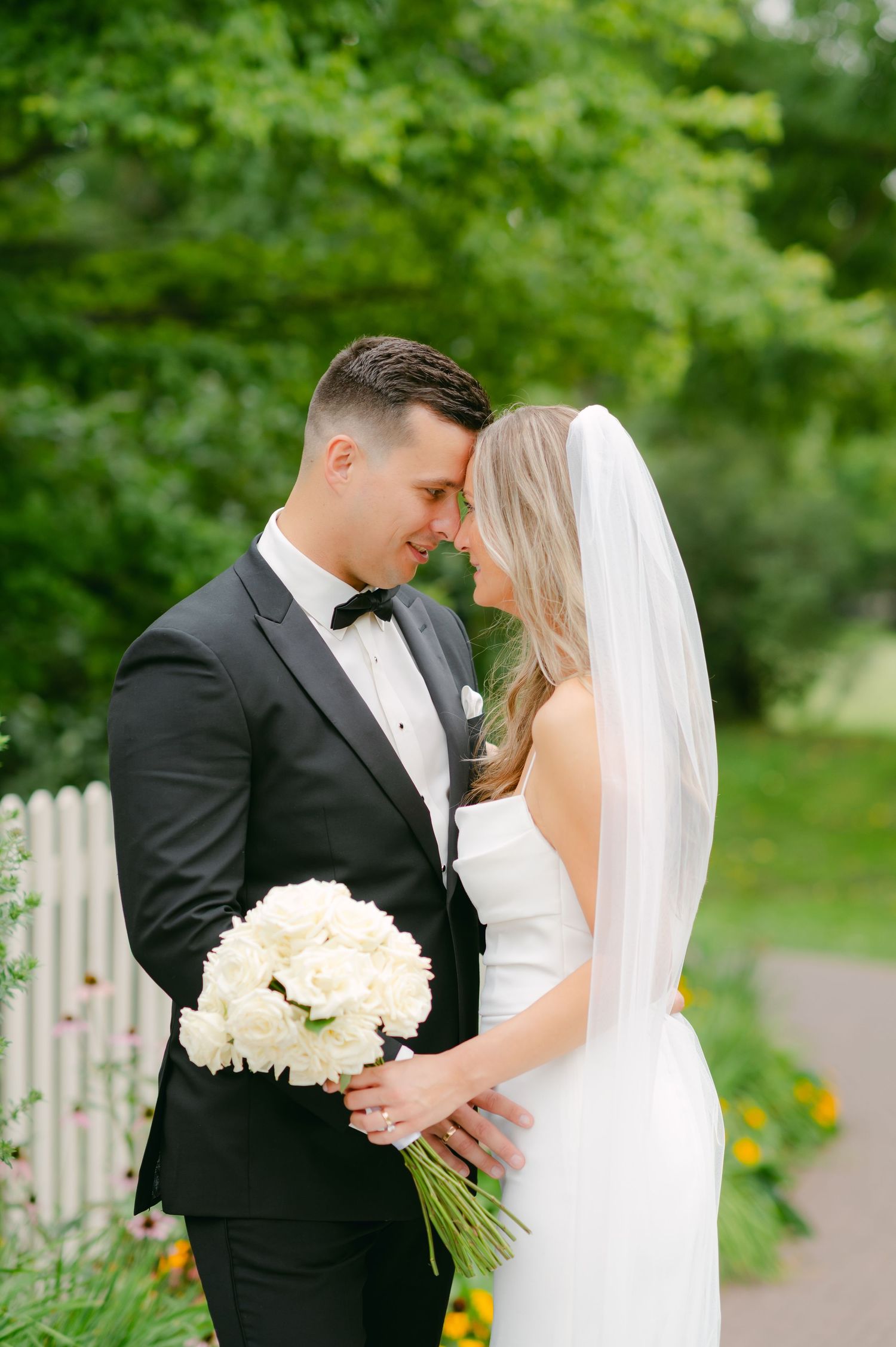 Intimate wedding moment captured in garden setting with beautiful white floral bouquet.