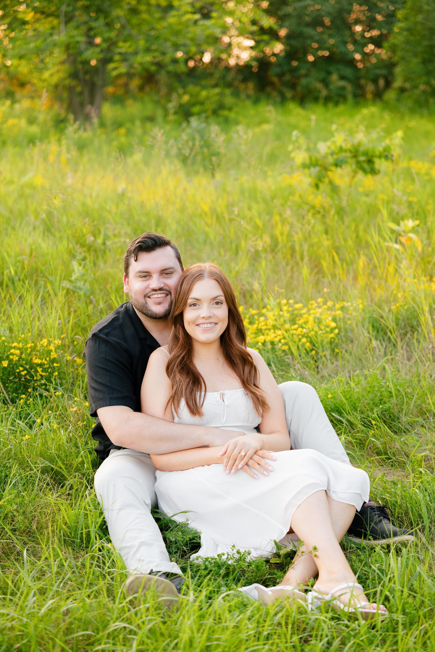 Couple sits together in blooming wildflower meadow during outdoor photoshoot.