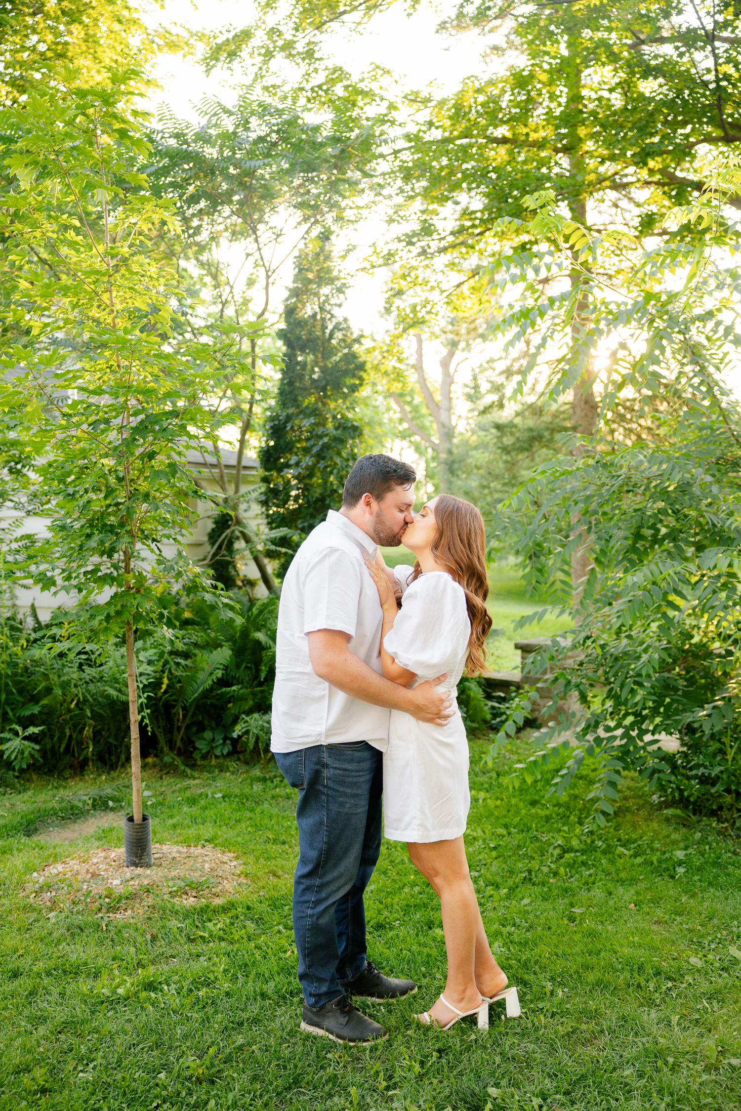 A romantic kiss shared between a couple in coordinating outfits surrounded by lush greenery.