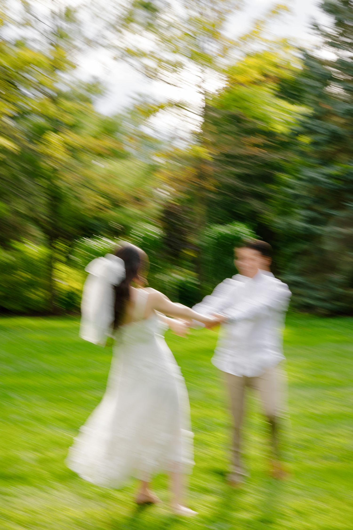A blurred motion shot of newlyweds dancing in a garden with vibrant green foliage.