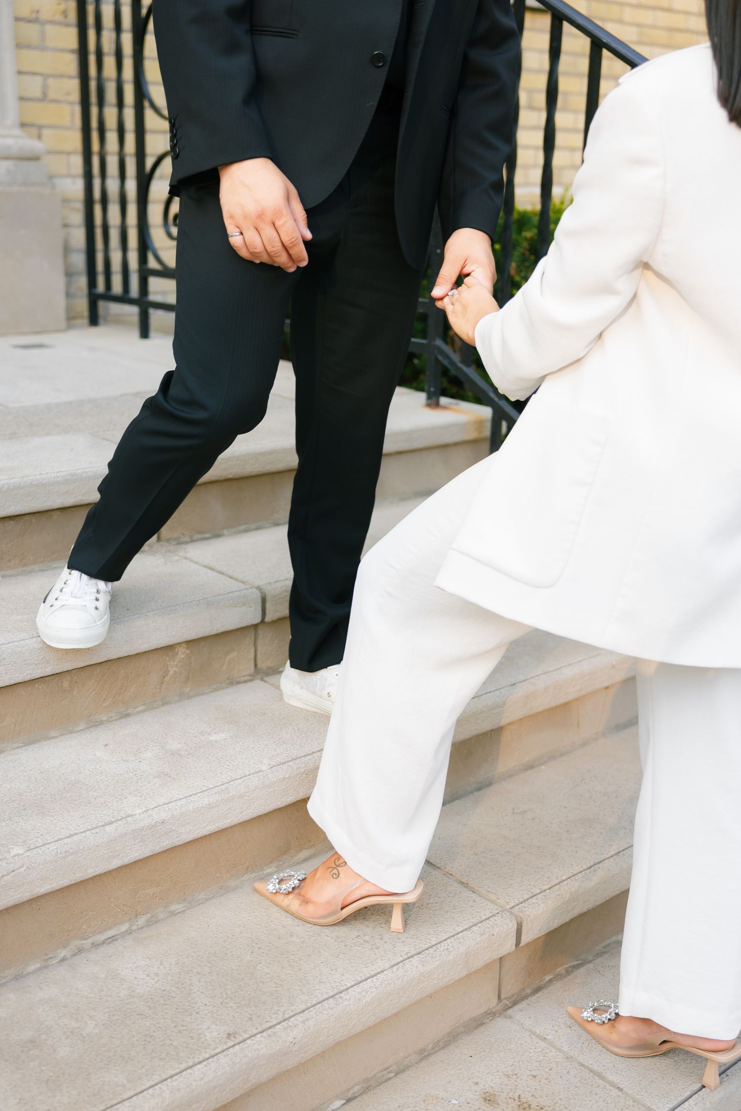 Close-up of contrasting footwear - white sneakers and nude heels on stone steps.