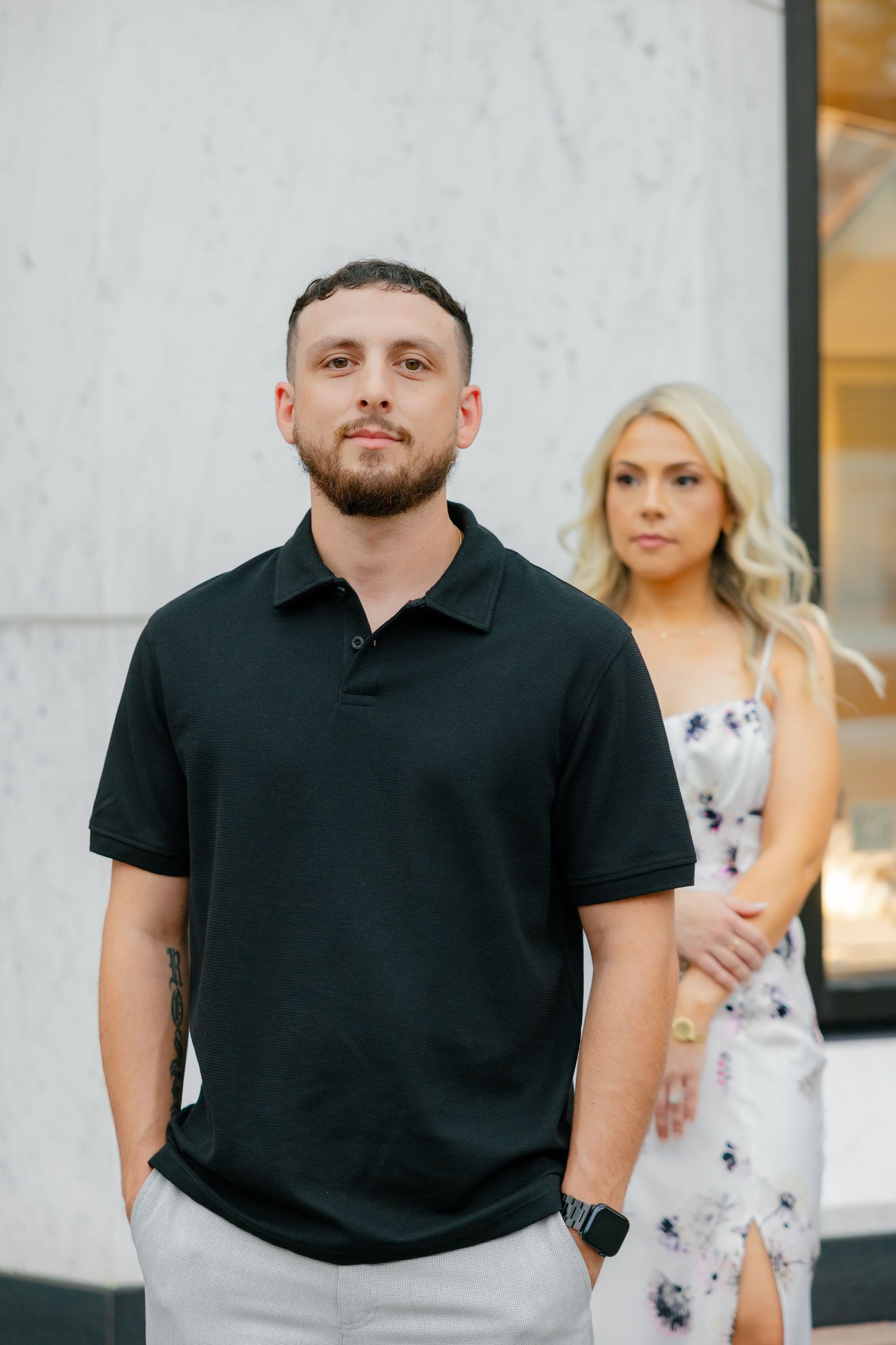 A stylish couple poses in front of a modern white marble wall wearing coordinated casual outfits.
