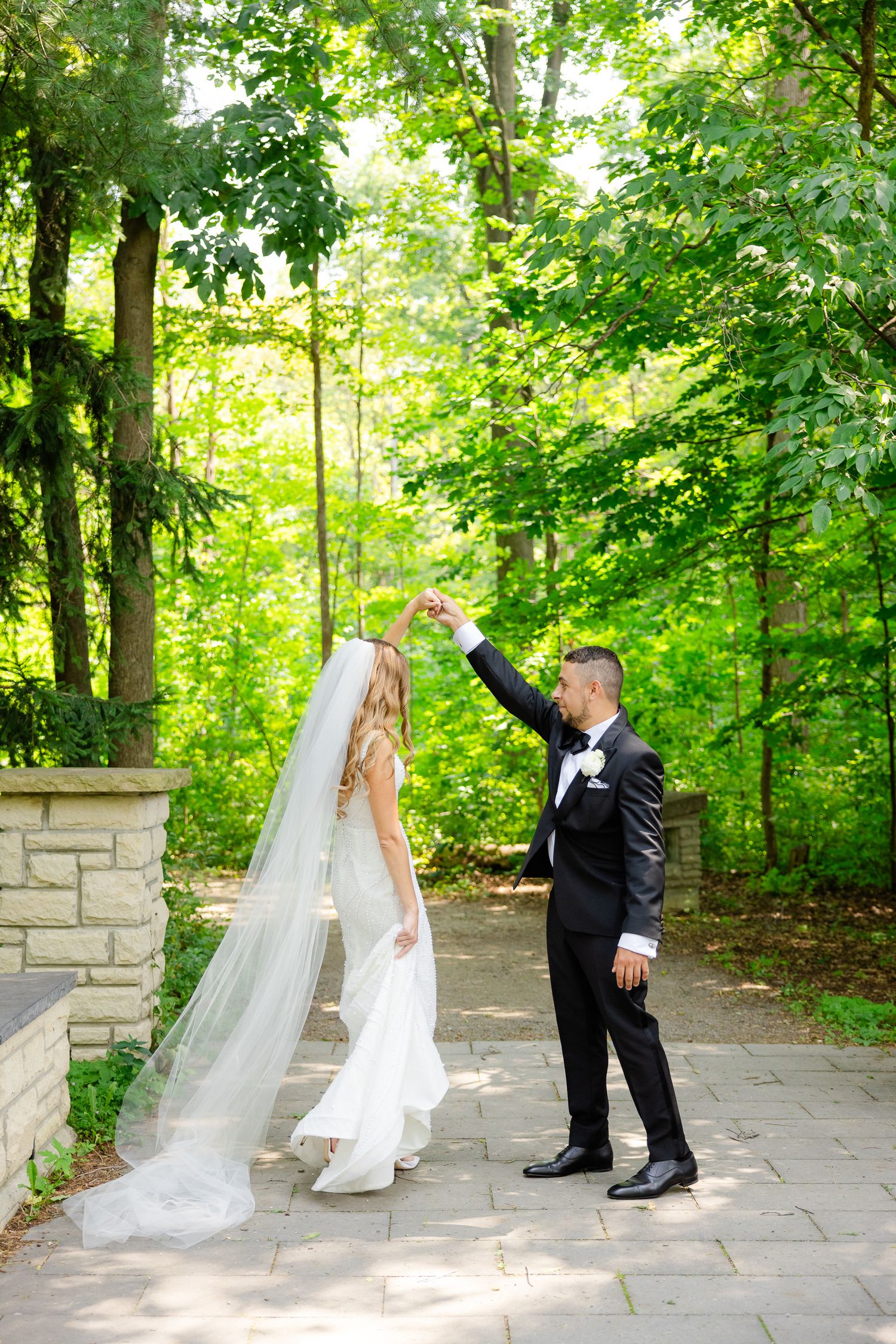 Wedding couple enjoying a playful moment on a stone path surrounded by lush green trees.