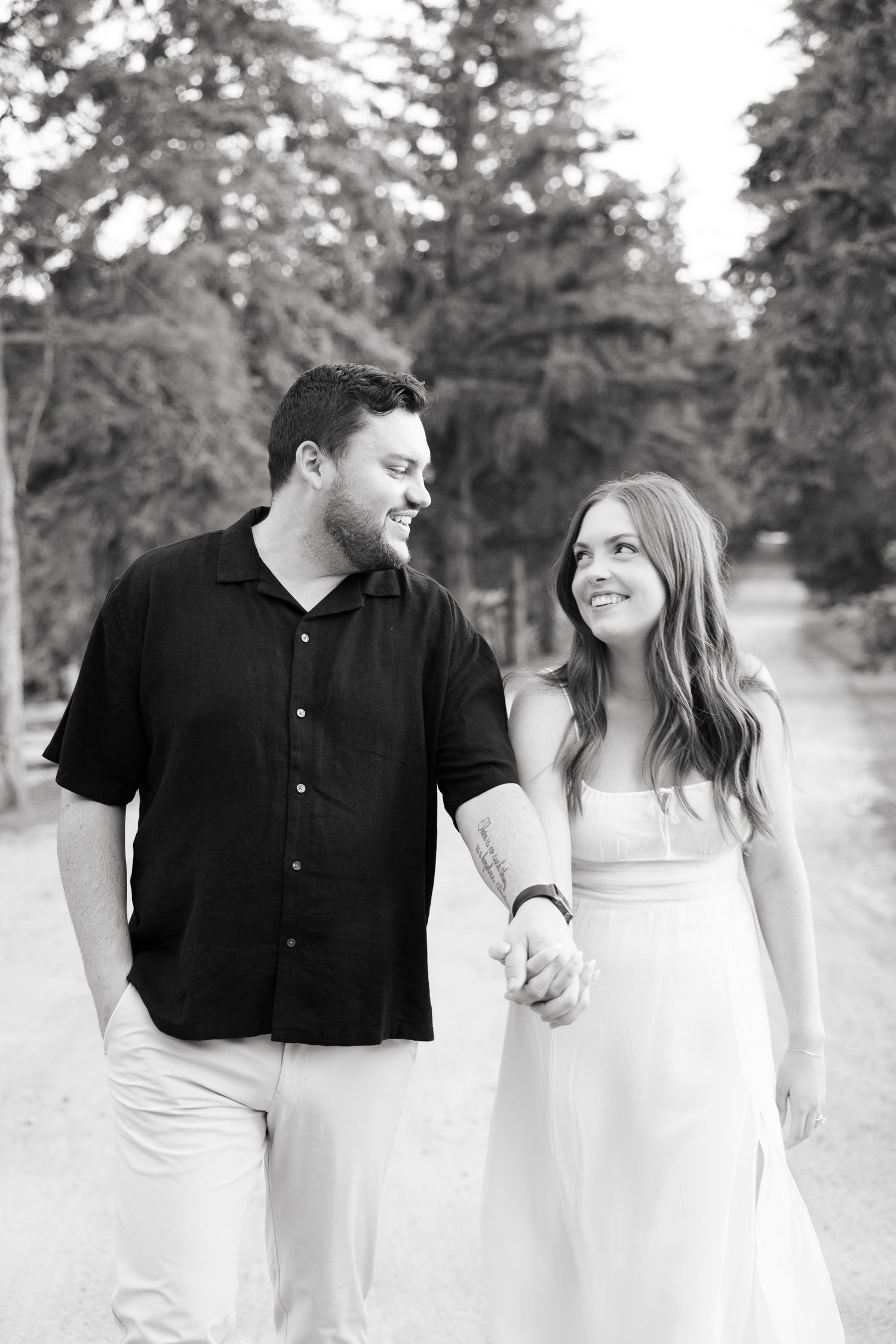A black and white portrait of a couple sharing a joyful moment on a wooded path.