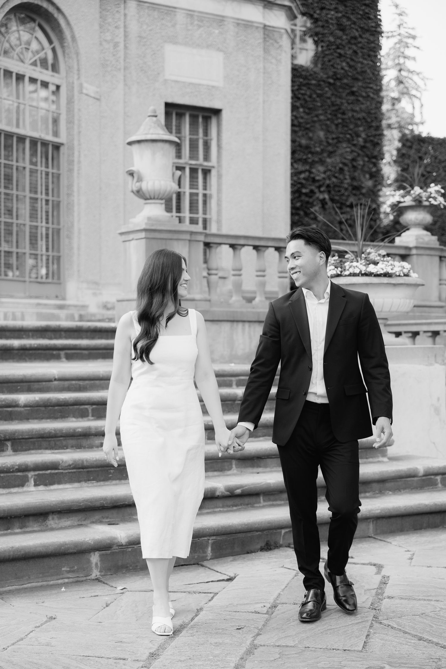 A couple holding hands while walking down ornate stone steps of a classical building.