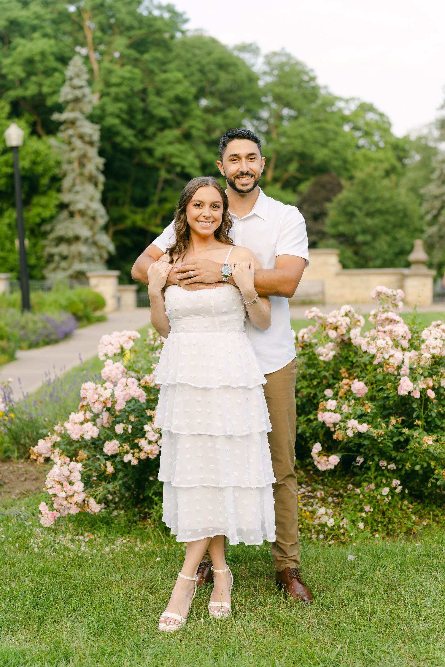 A romantic engagement photoshoot in a garden with blooming pink roses and stone architecture.