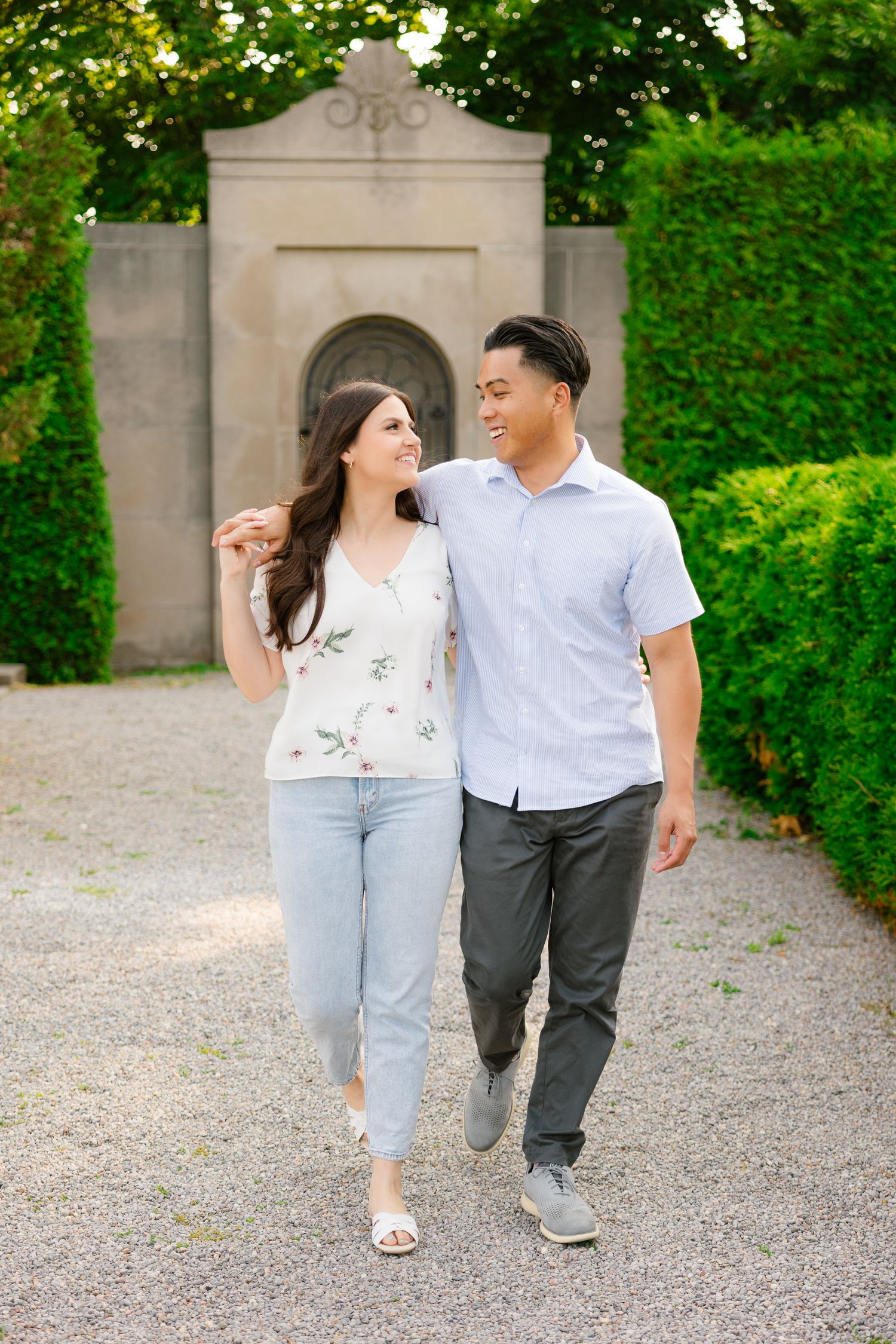 A couple takes a romantic stroll along a garden path with a decorative stone wall backdrop.