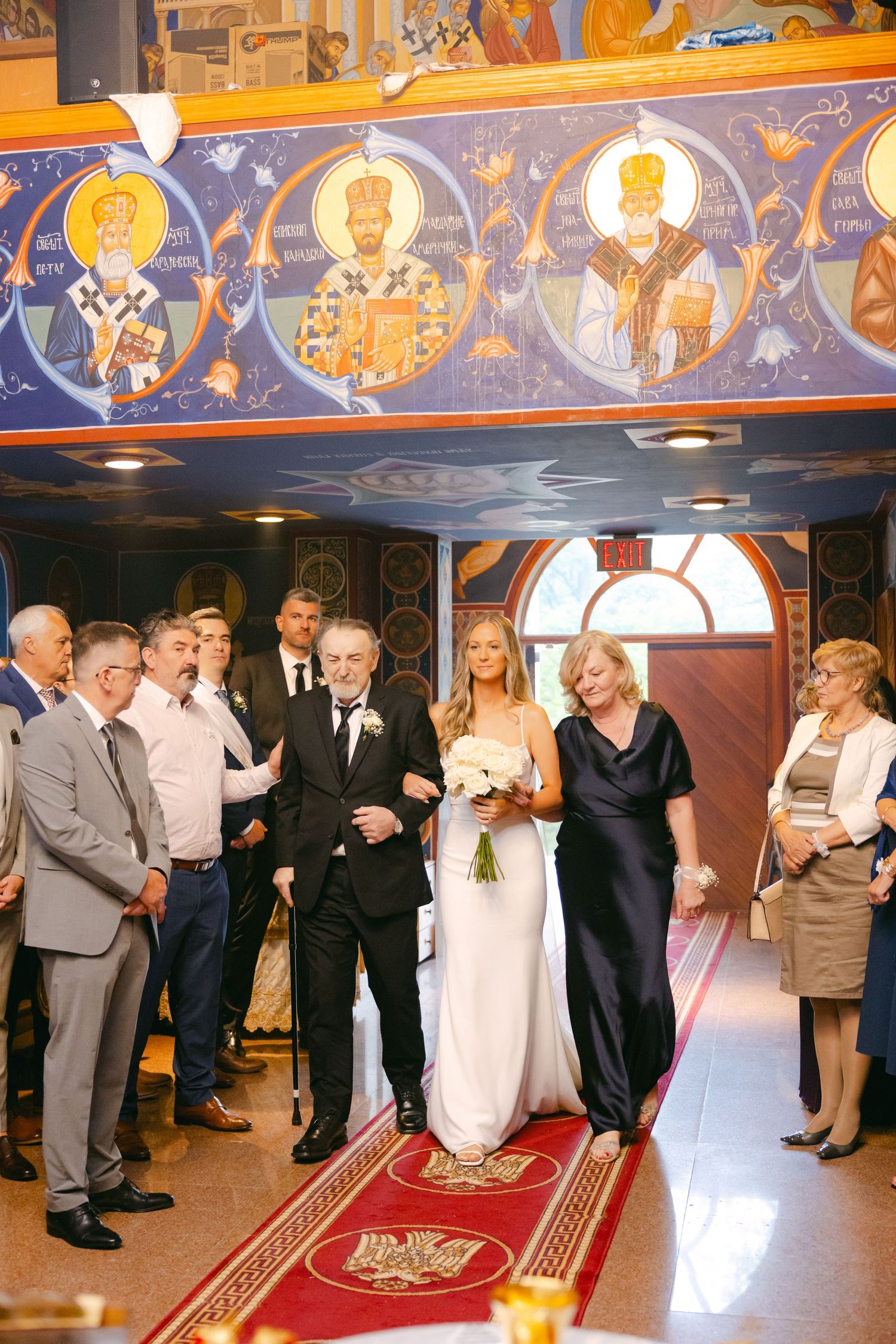 Wedding ceremony taking place in an Orthodox church with ornate religious icons and frescoes adorning the walls.