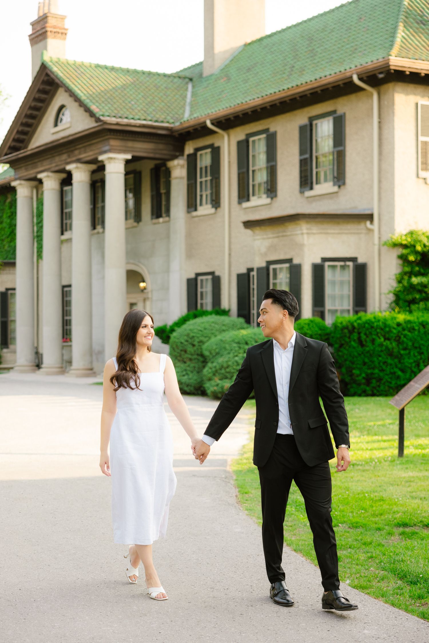 Couple strolls hand in hand along pathway by classic colonial architecture.