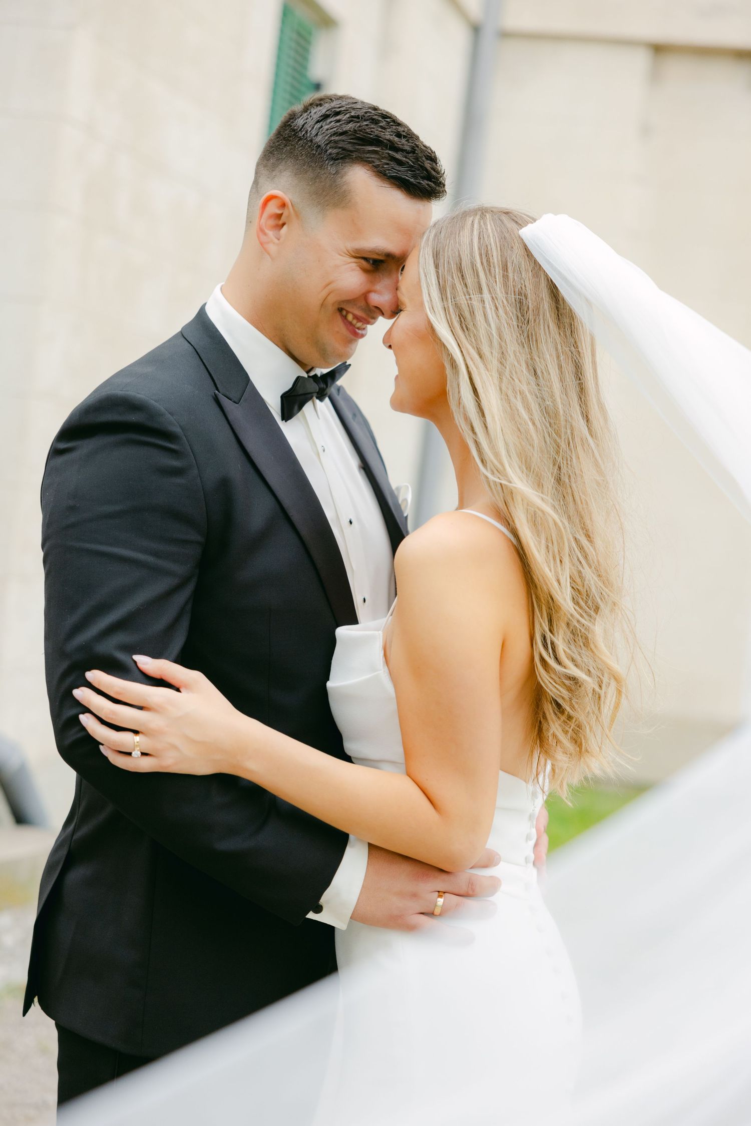 Elegant wedding couple sharing an intimate moment against a neutral building exterior.
