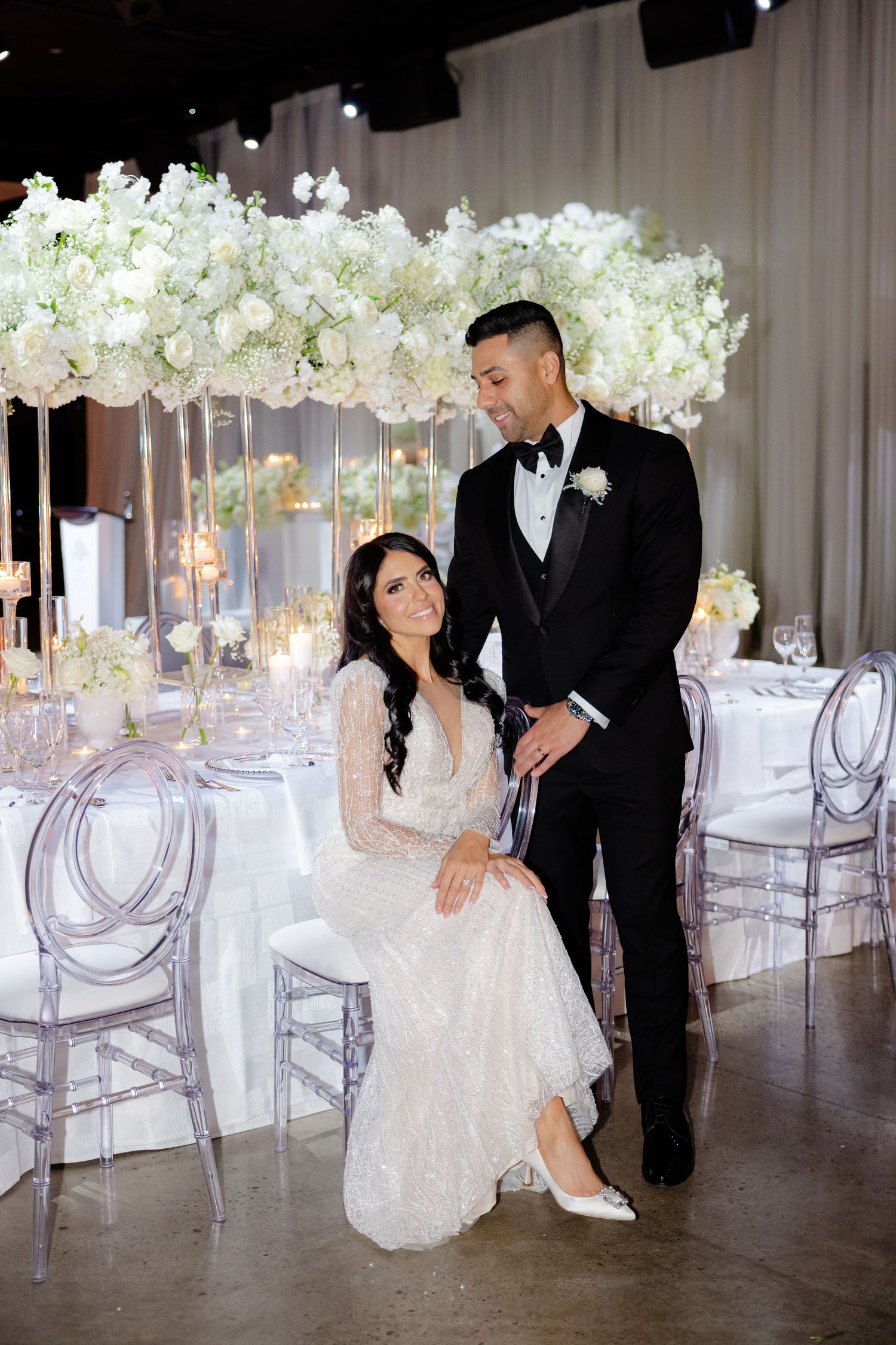 Wedding couple posing by luxurious table settings with suspended white floral arrangements.