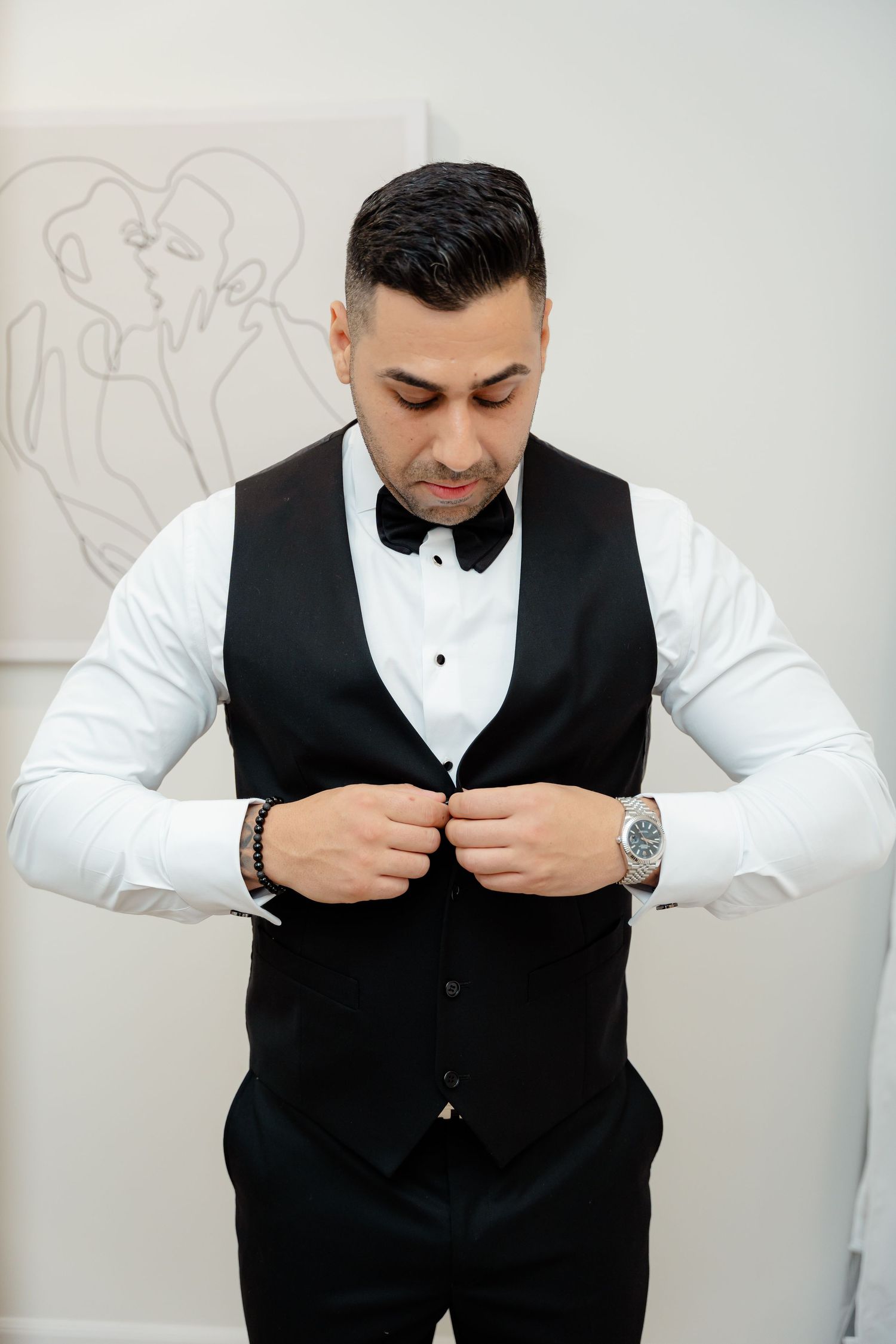 Groomsman in classic black vest and bow tie buttoning up formal wear.