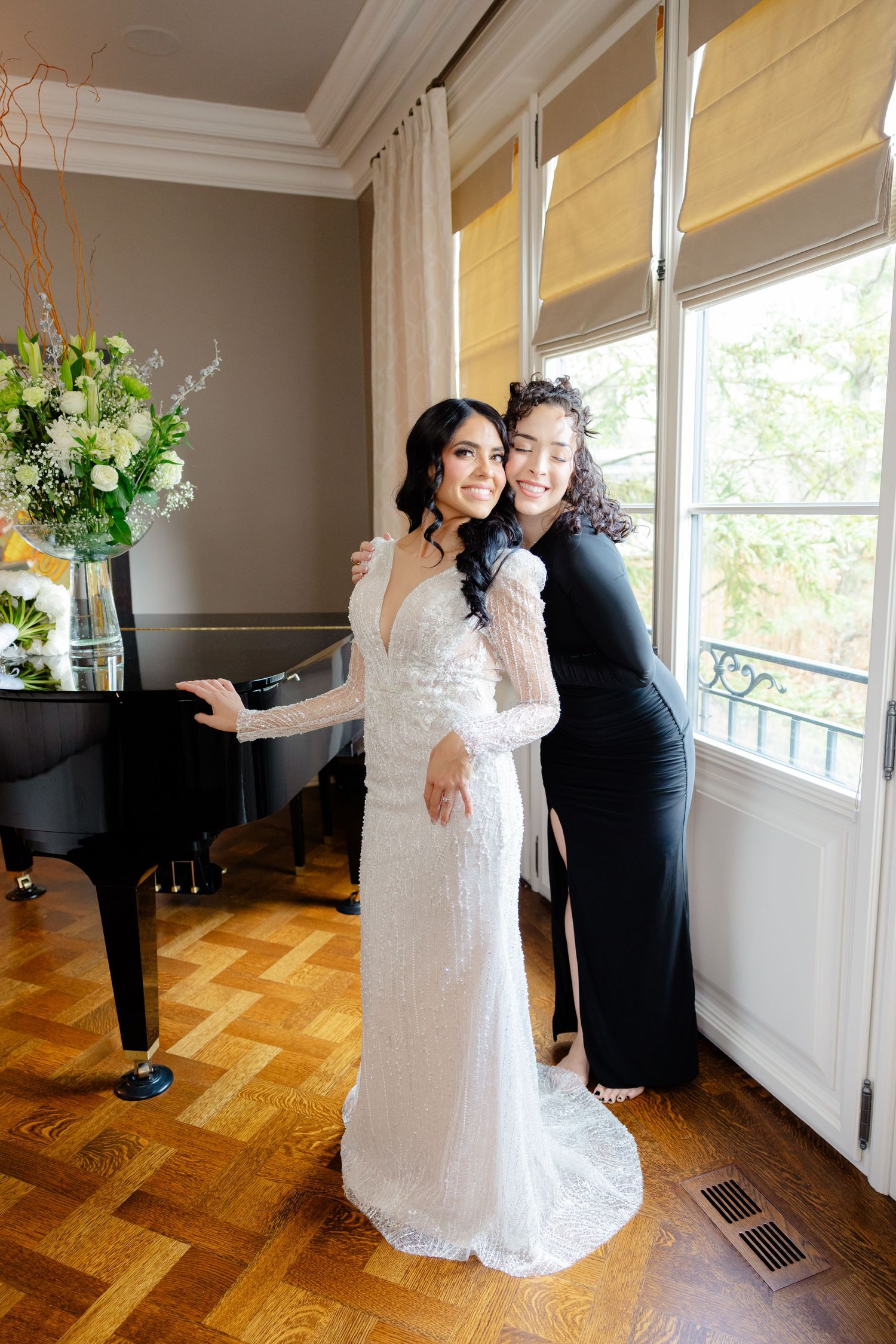 Wedding dress fitting session by windows with grand piano and floral arrangement.