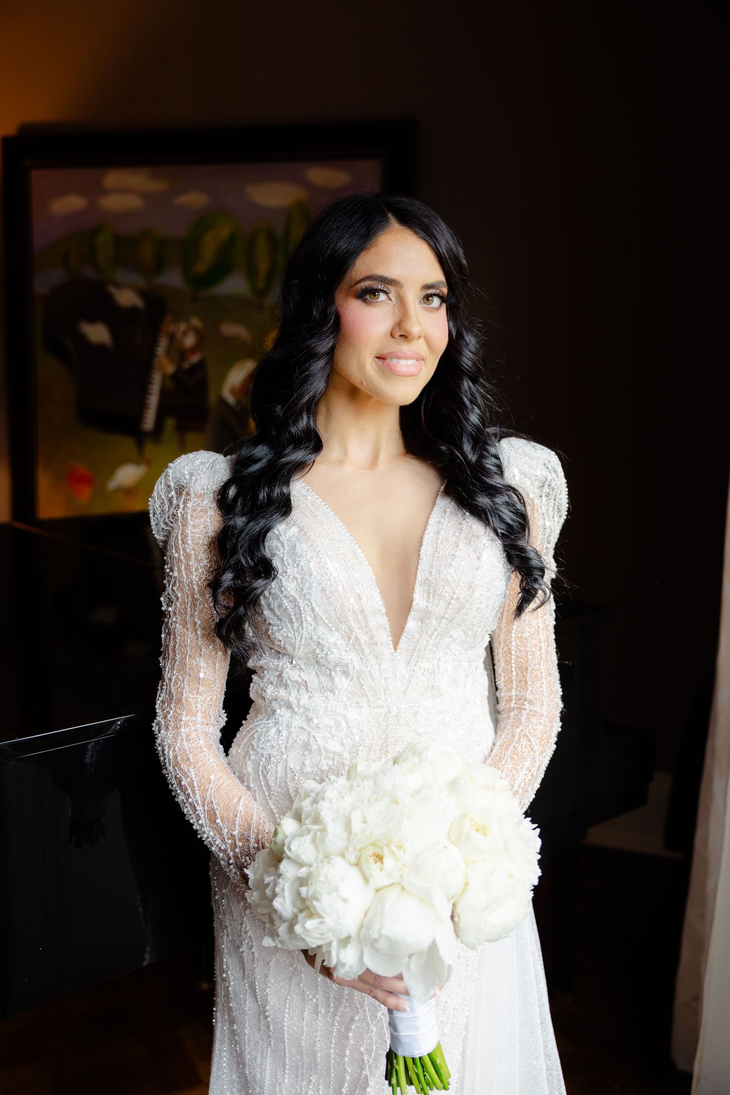 Stunning bridal portrait with plunging neckline lace gown and white bouquet against dark background.