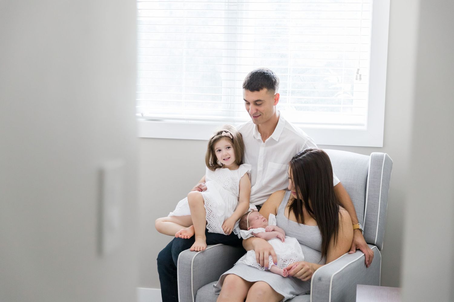 Family of four sharing intimate moments together on a comfortable grey chair.