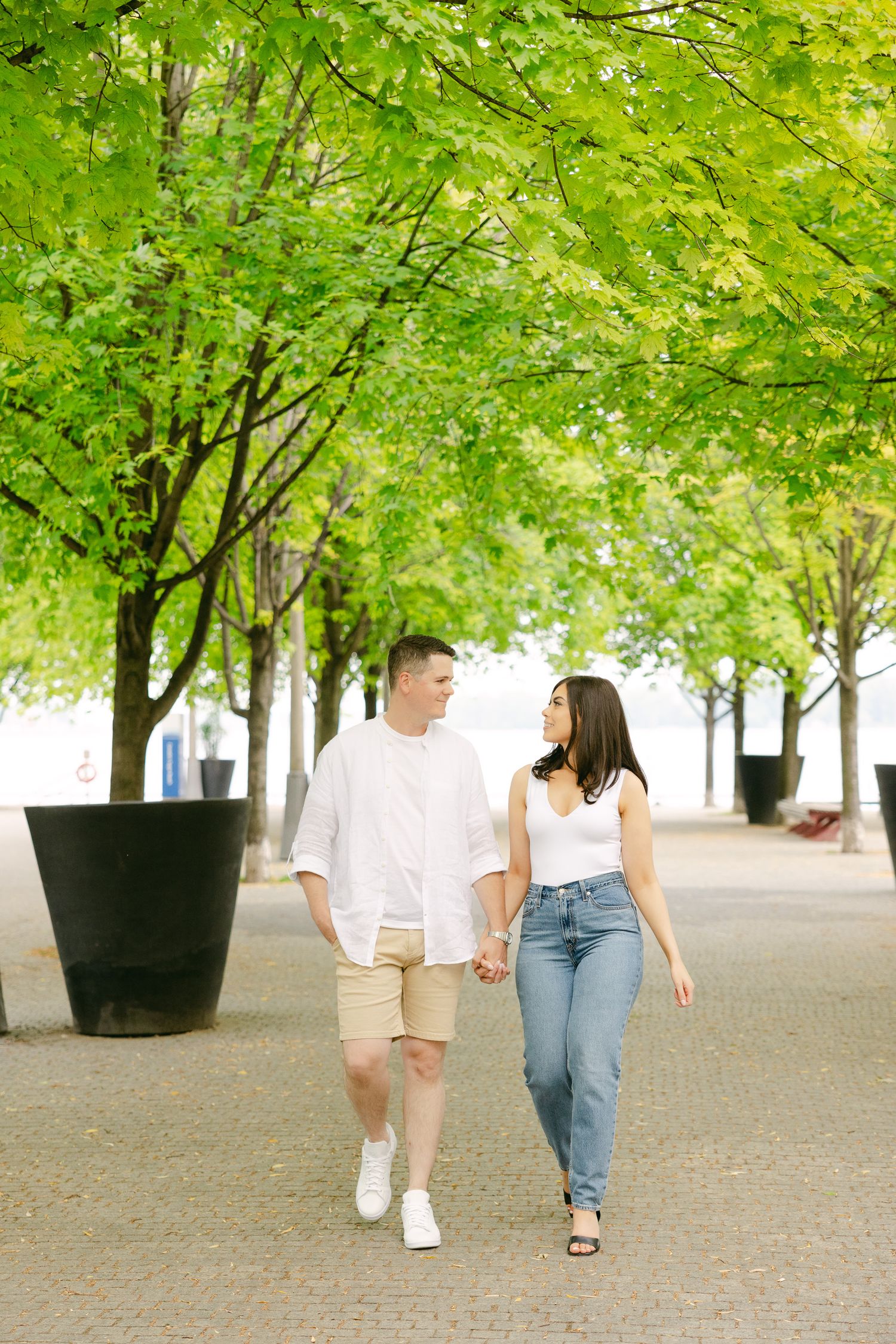 Two people walk together holding hands beneath a canopy of green leaves.
