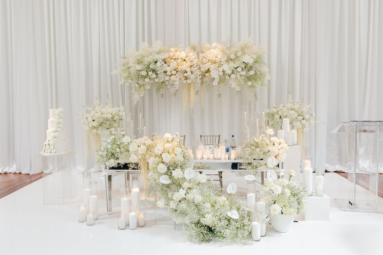 Romantic white floral arch display with candles and glass accents.