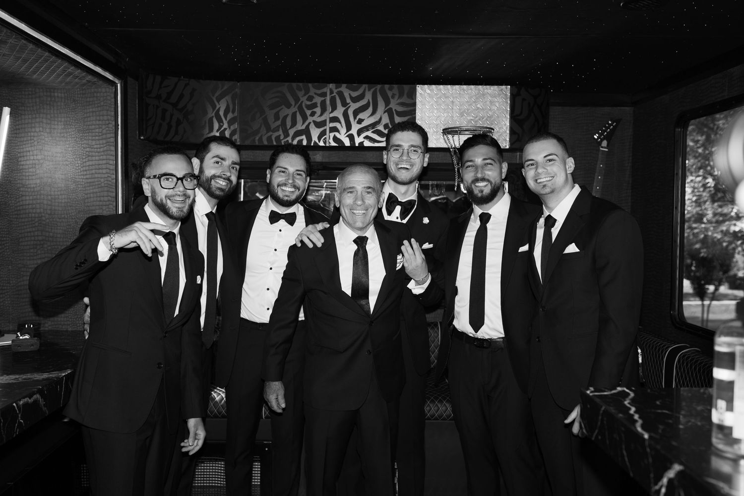 Group in formal attire posing together inside a dimly lit venue with decorative wall art.