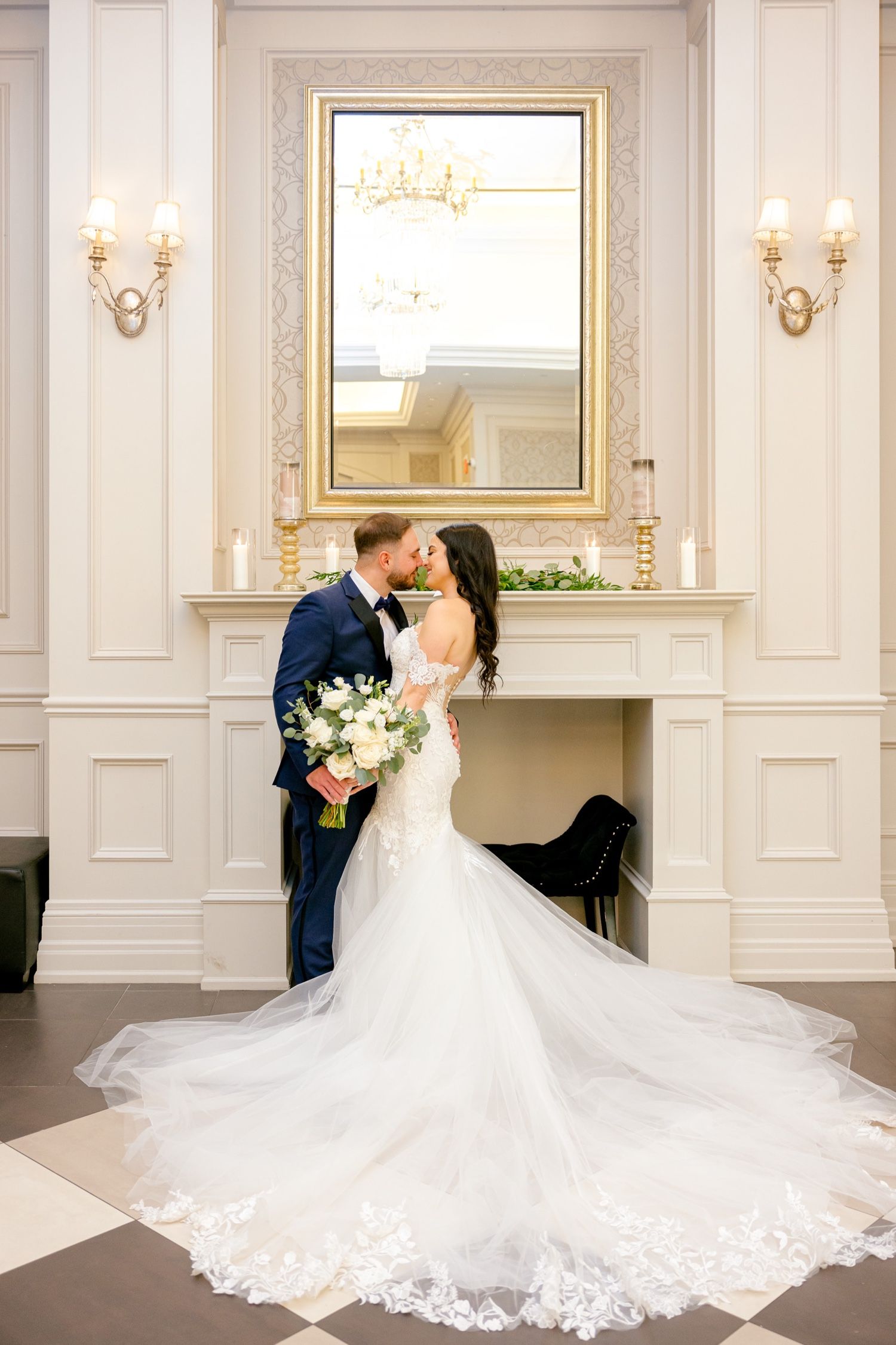 Romantic wedding portrait in front of ornate gold mirror and white paneled walls.