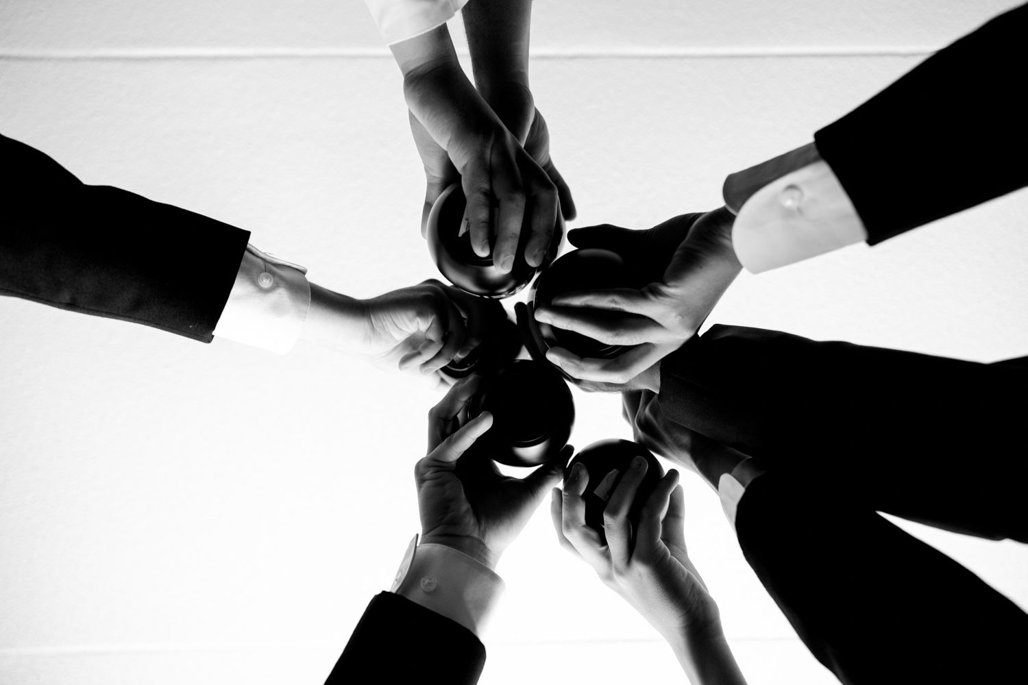 Artistic black and white shot of hands joining together in a circle wearing formal suit sleeves.
