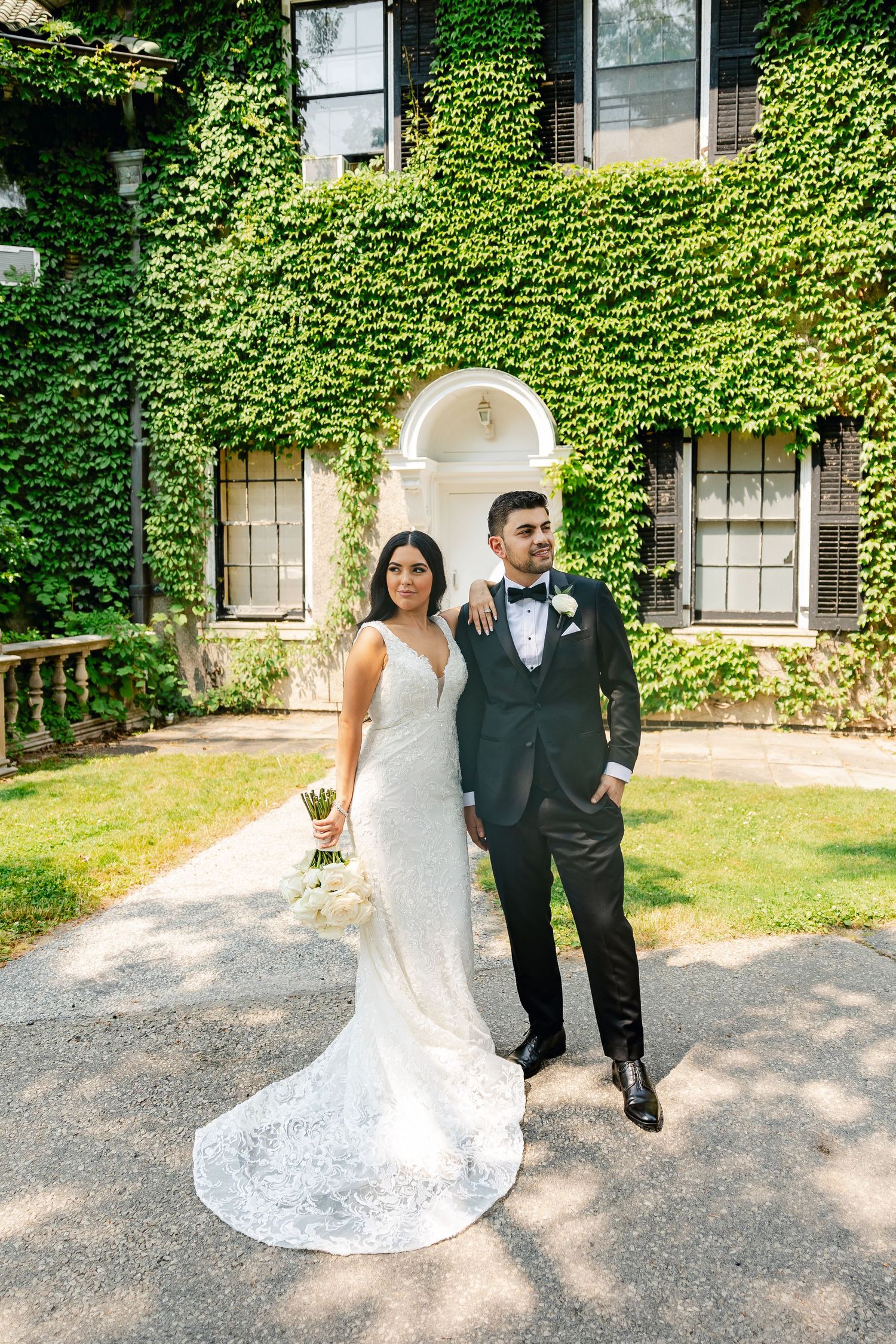 Wedding couple poses in front of an elegant ivy-covered building with classic architecture.