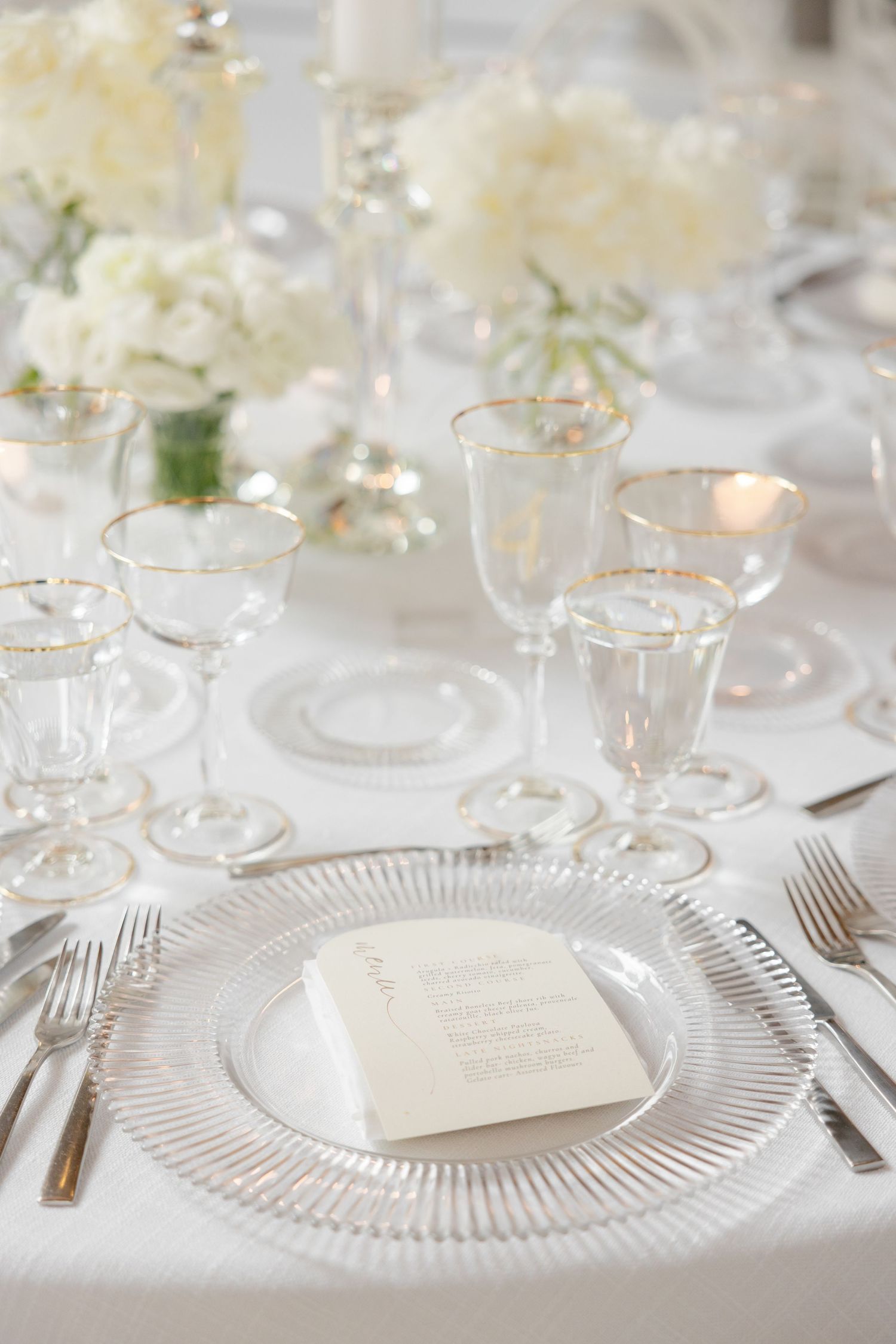 Formal place setting with crystal charger plate, white menu card, and delicate glassware.