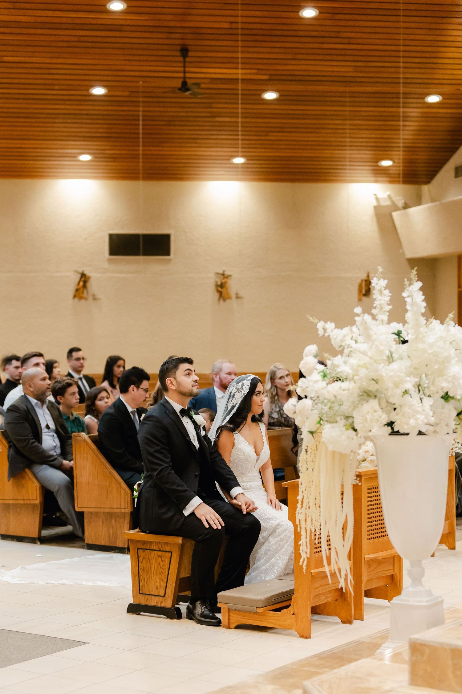 Wedding ceremony in a church with white floral decorations and wooden ceiling.