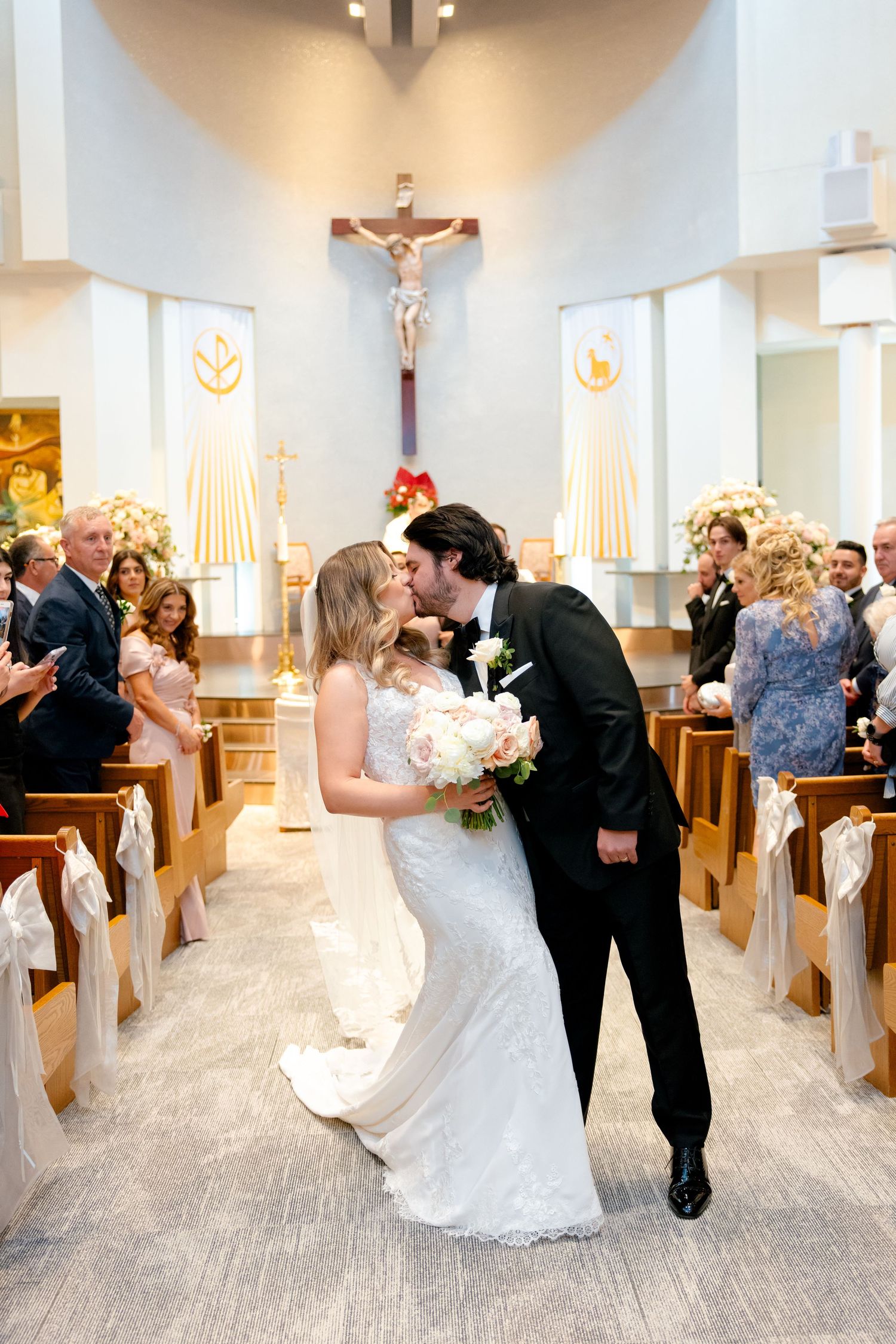 Wedding couple sharing their first kiss in a church aisle surrounded by guests.