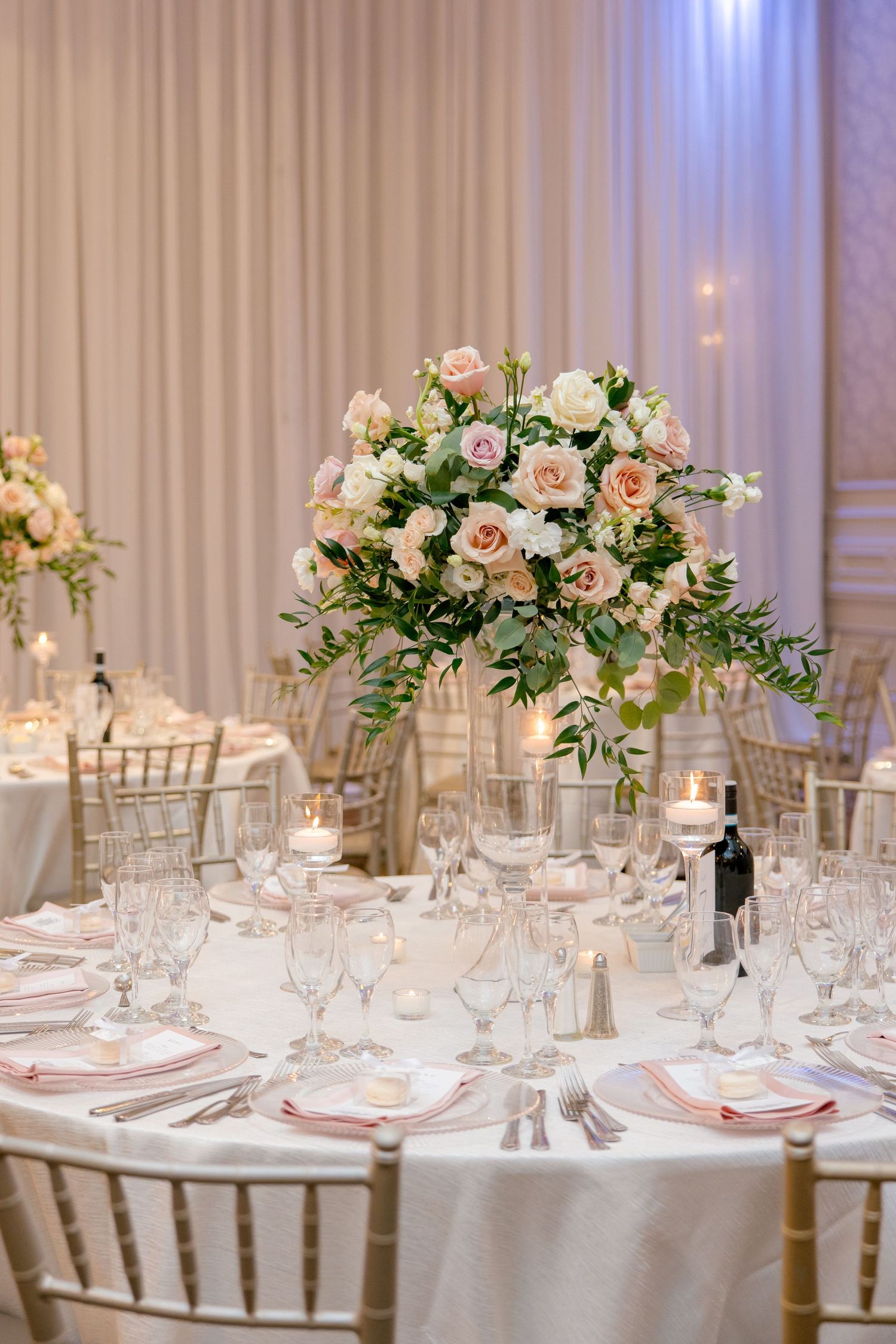 Luxurious wedding centerpiece with blush roses and white flowers atop elegant table setting.
