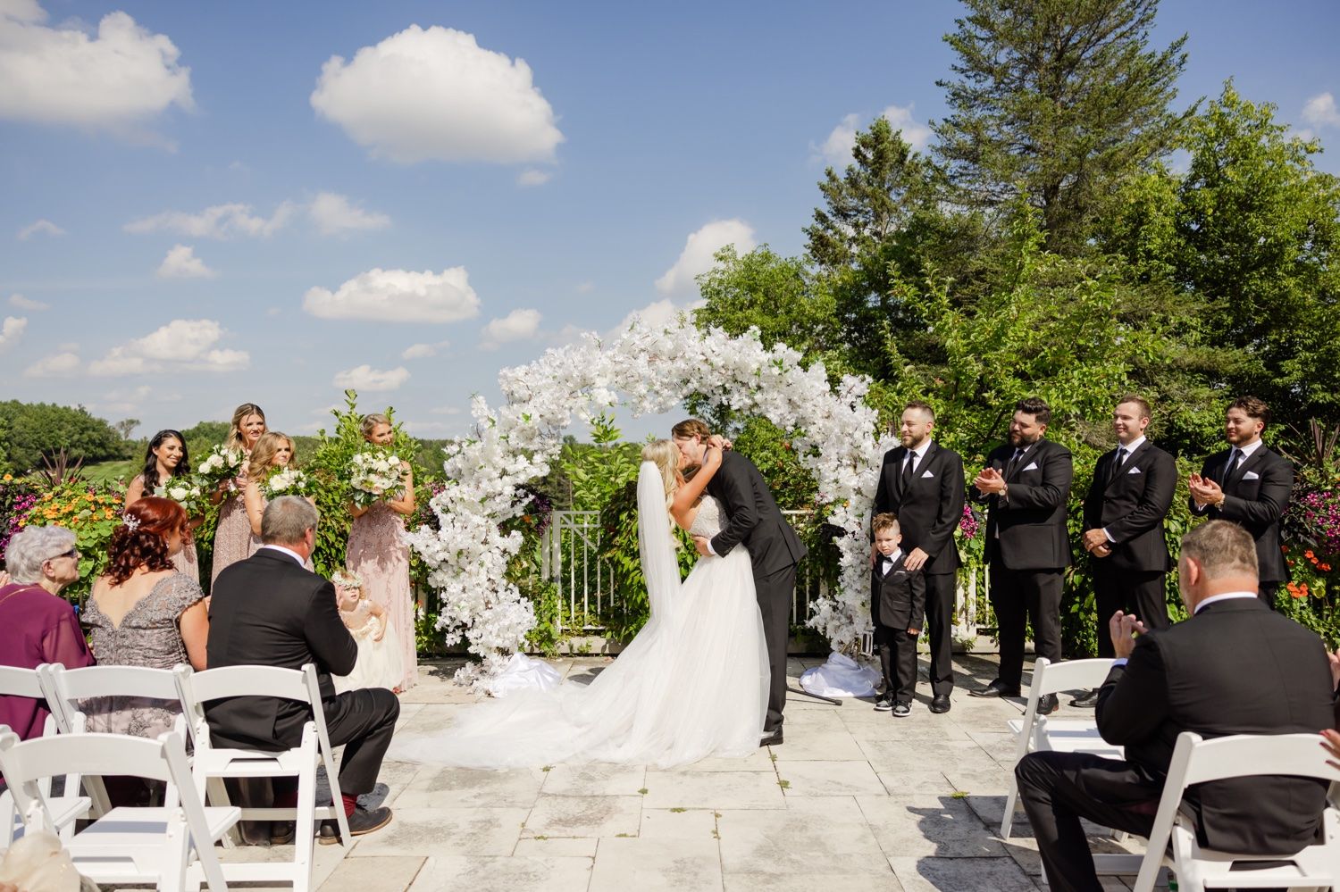 Joyful wedding celebration with guests watching the ceremony under a white floral archway.
