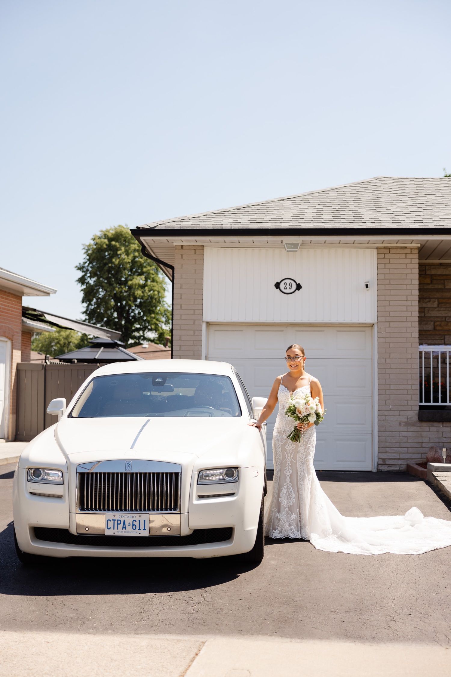 A luxurious white Rolls Royce parked in front of a residential garage during a wedding photoshoot.