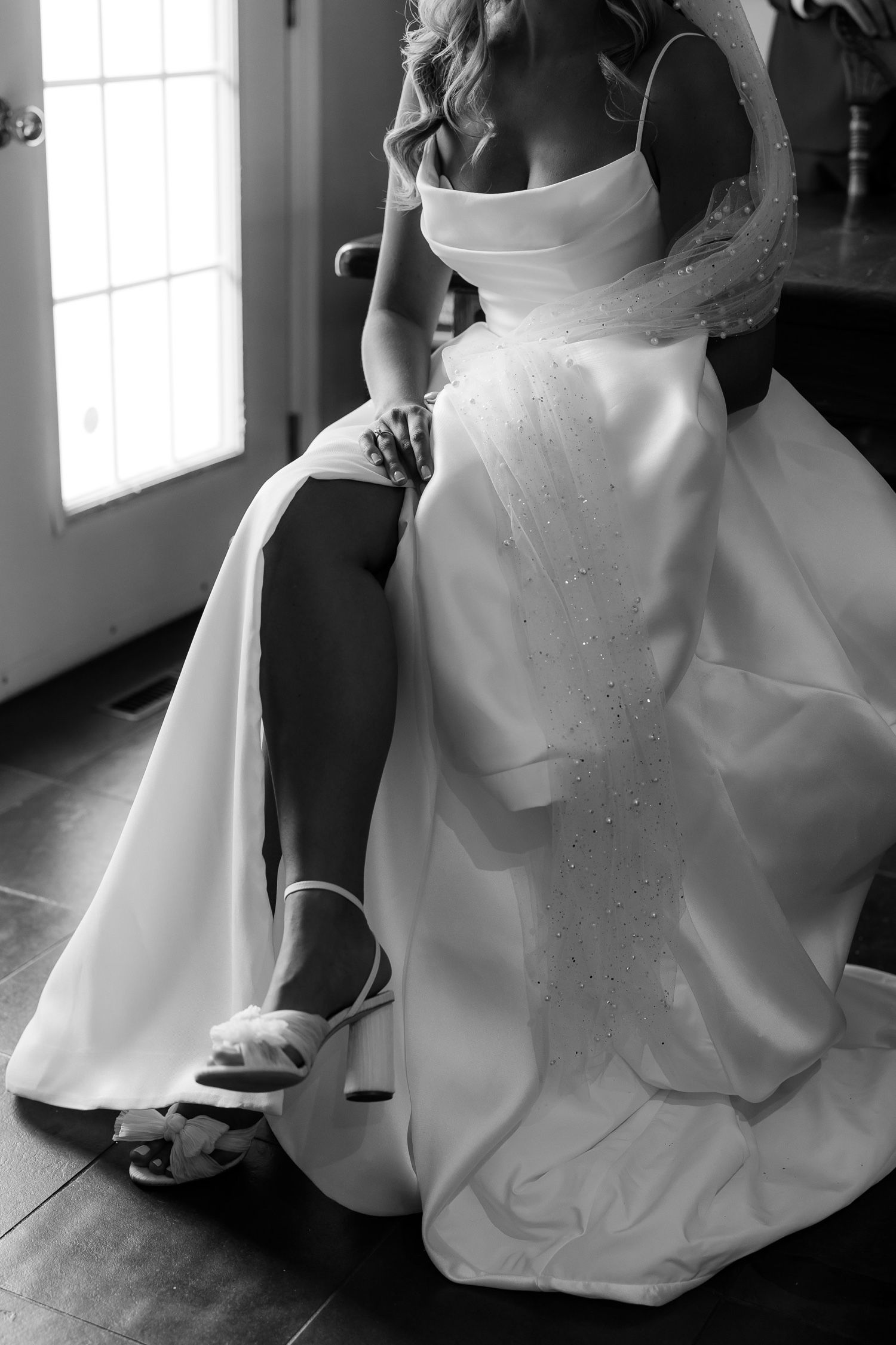 Black and white photo of a wedding dress detail with sparkly embellishments and white shoes on a wooden floor.