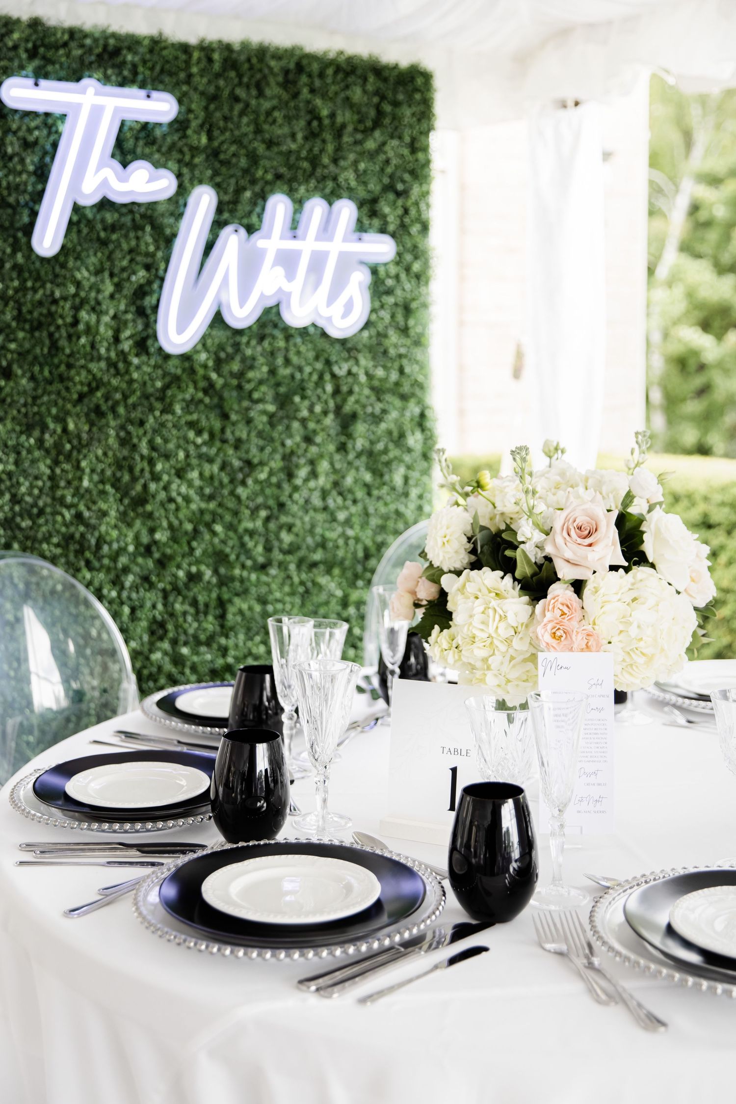 Wedding table with neon sign, boxwood wall, and black and white place settings.